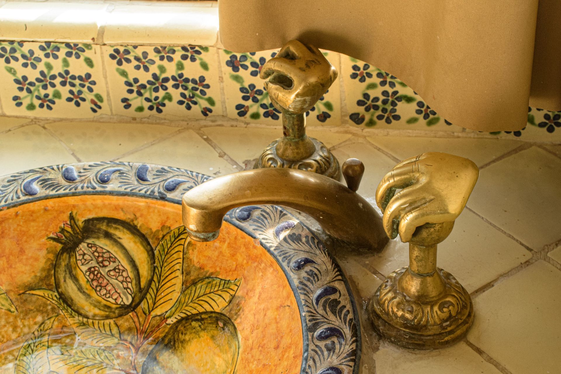 Primer plano de un lavabo decorativo con grifo y manijas doradas ornamentadas. Diseño floral pintado en el lavabo.