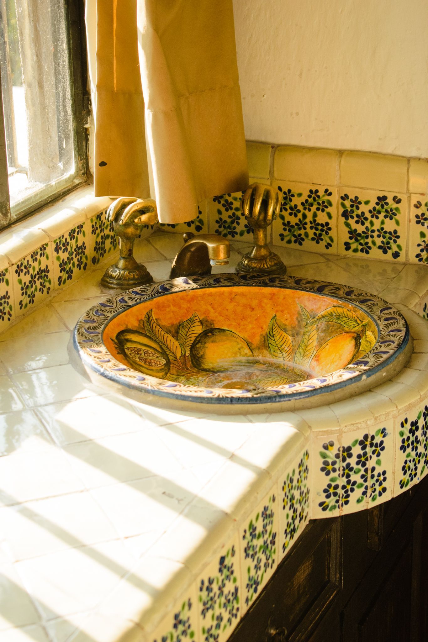 Lavabo de baño con lavabo decorativo de color naranja, grifo dorado y encimera con azulejos florales.