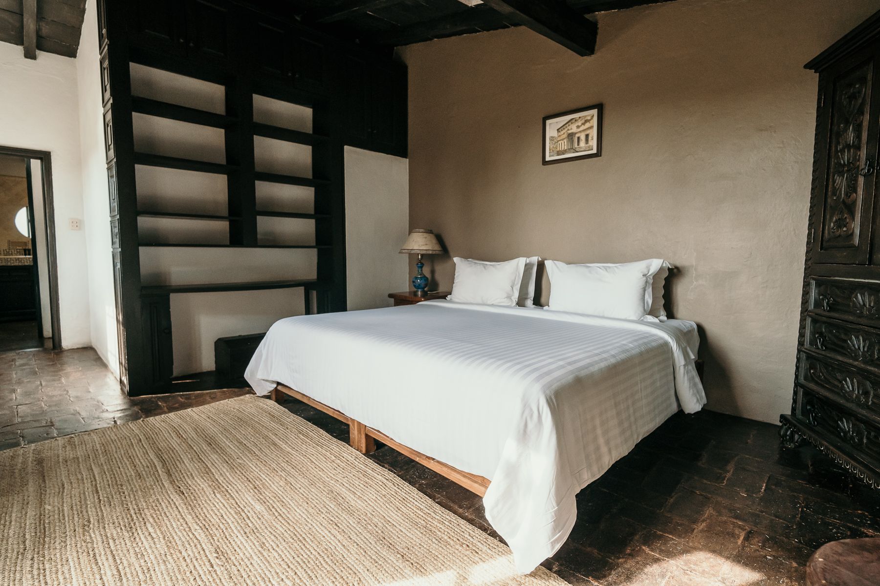 Dormitorio con cama, alfombra, estanterías empotradas, muebles de madera oscura y una pared en tono neutro.