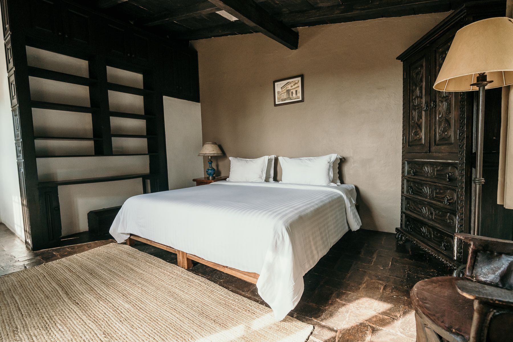 Dormitorio con ropa de cama blanca, alfombra, muebles de madera y lámpara de pie.