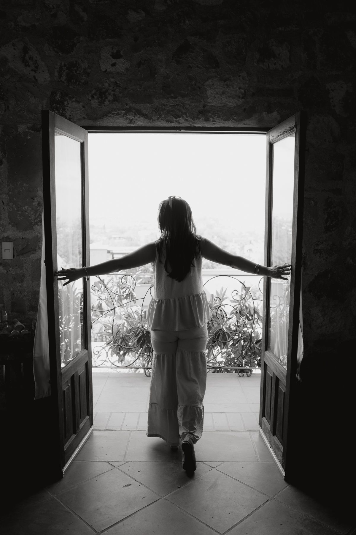 Mujer con los brazos extendidos en el umbral, contemplando un paisaje. Blanco y negro.