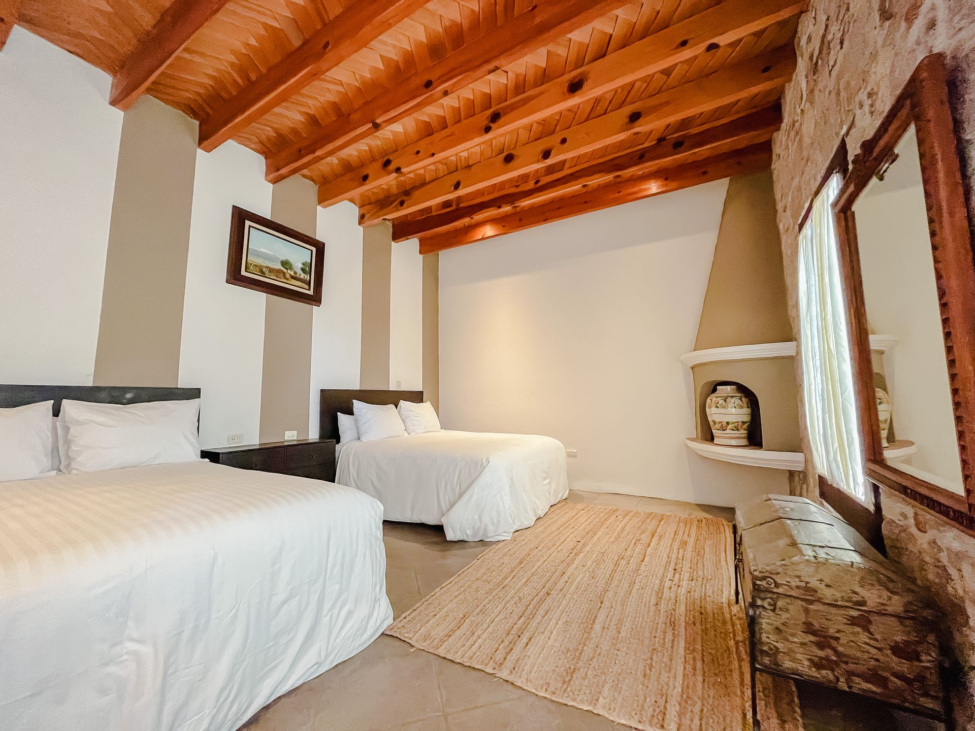 Dormitorio con dos camas, techo de madera, pared de piedra, chimenea y espejo.