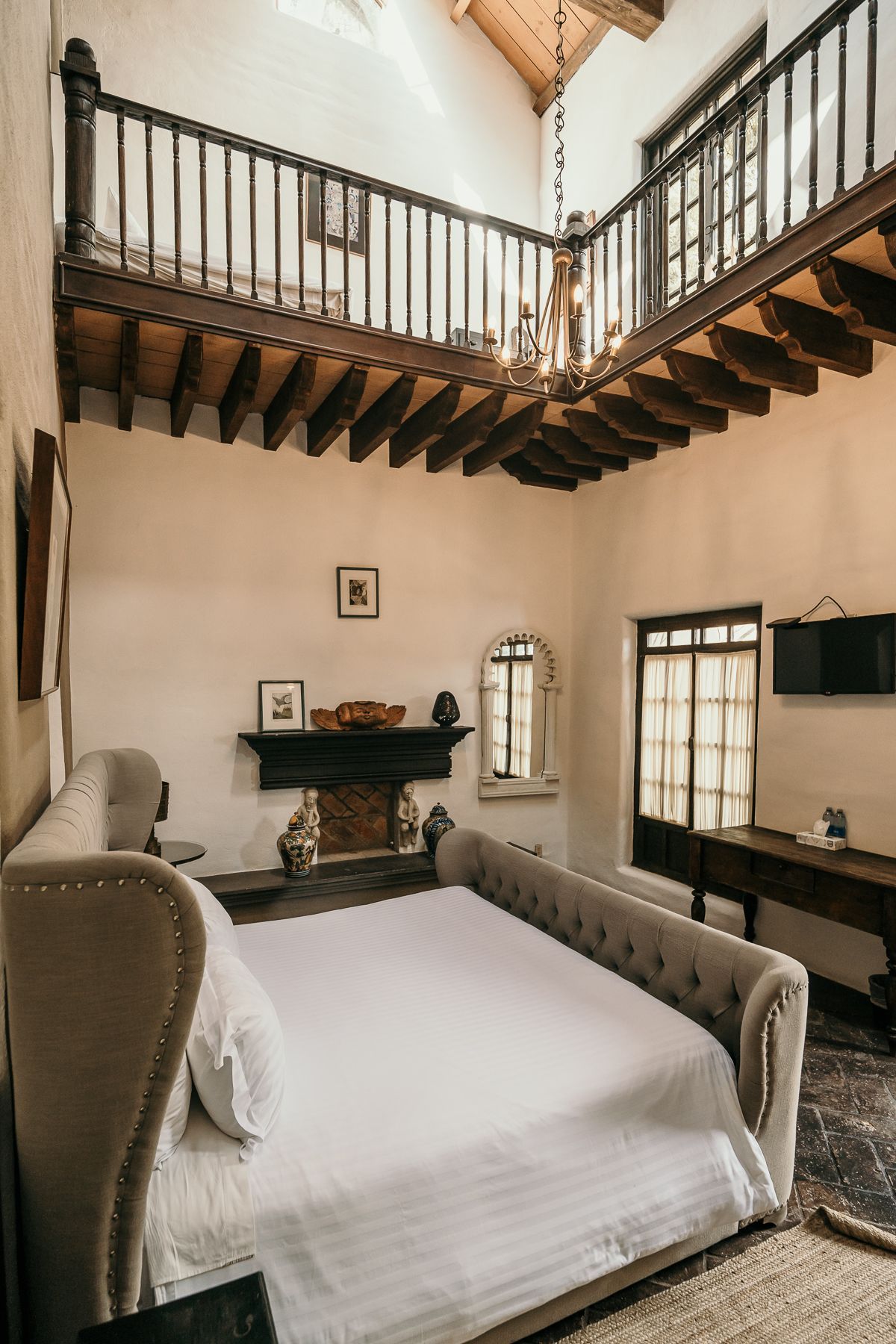 Dormitorio con entrepiso, cama en primer plano, chimenea, ventana y balcón de madera oscura.