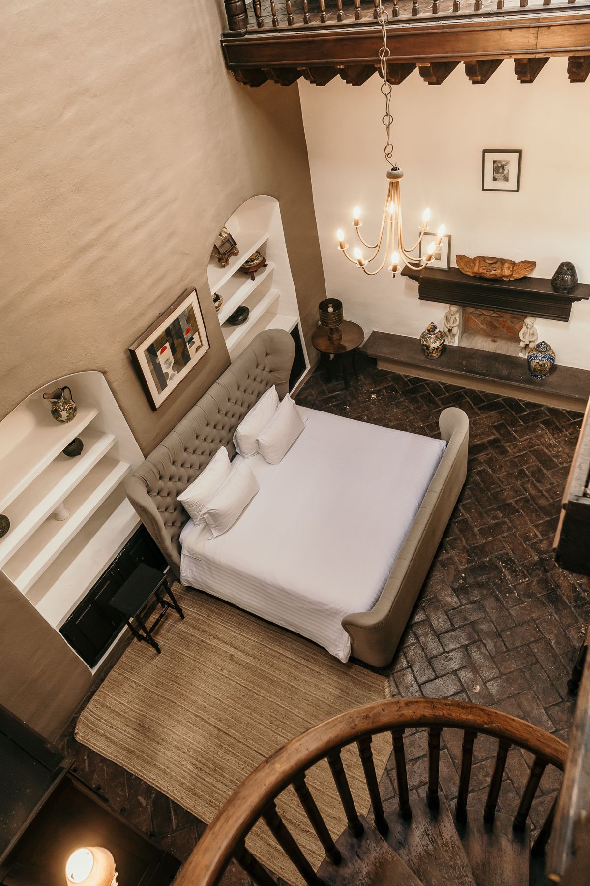 Dormitorio con techos altos, cama, alfombra, chimenea, lámpara de araña y vista a la escalera de caracol.