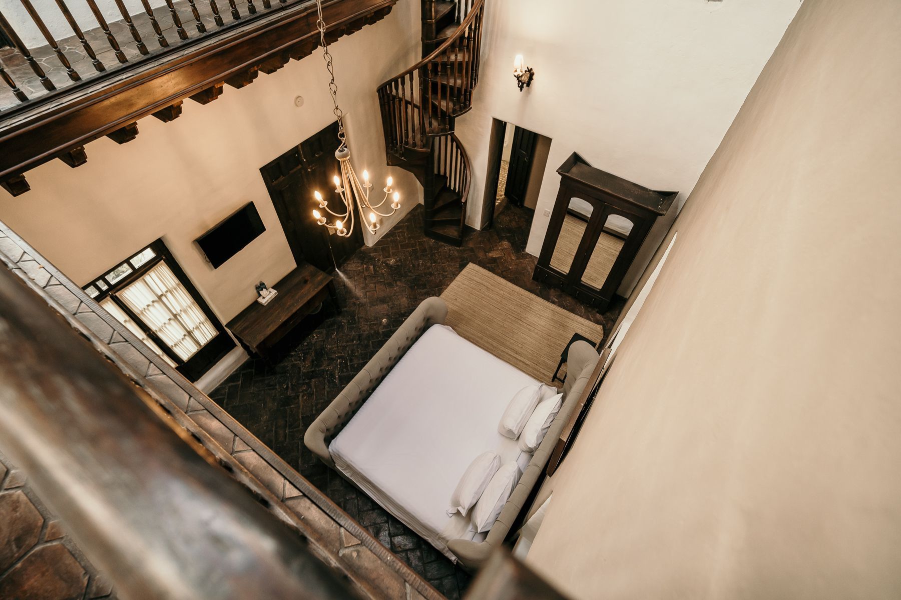 Interior de dormitorio con cama, lámpara de araña, escalera de caracol y detalles en madera oscura.