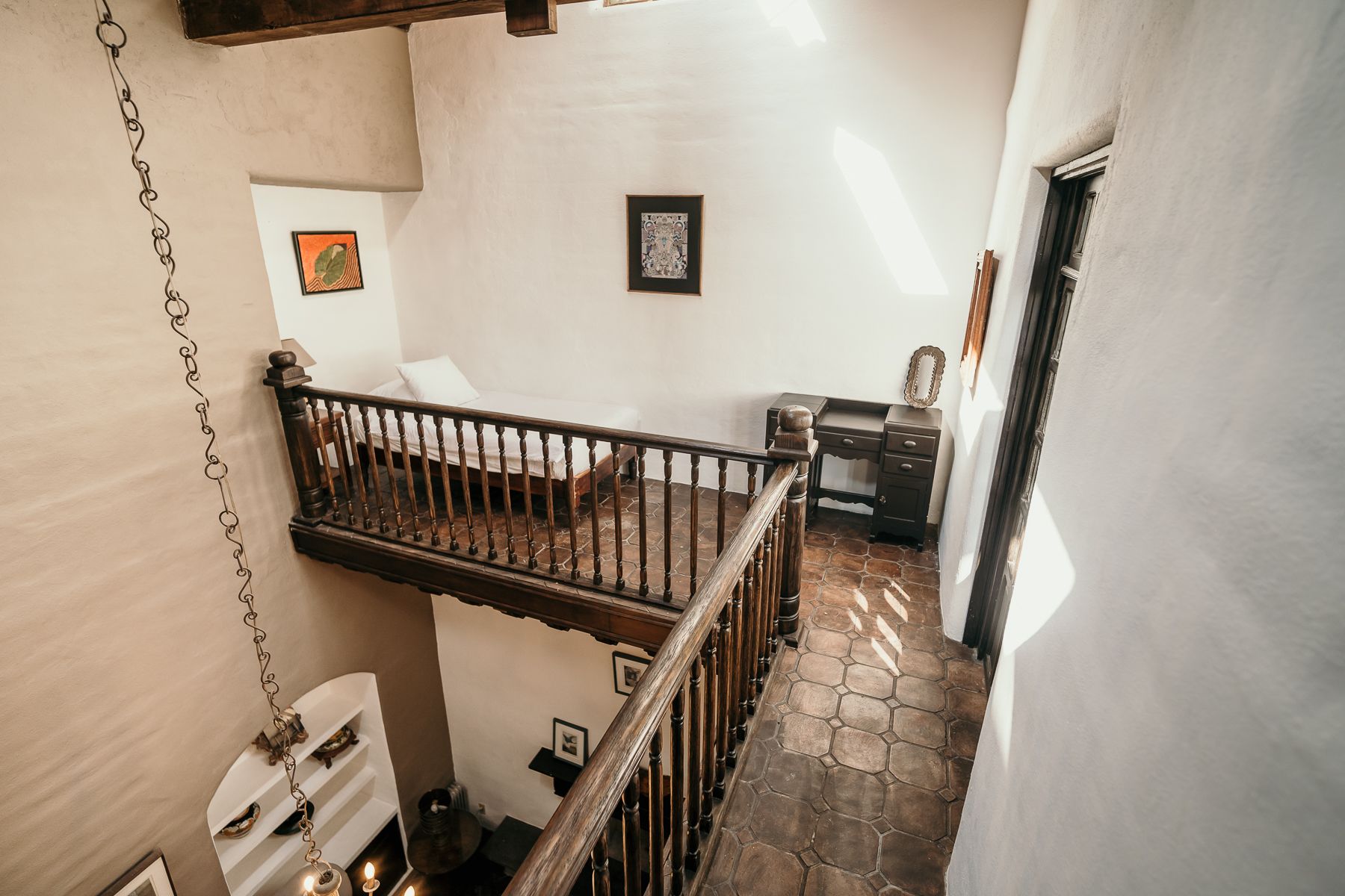 Vista interior de un balcón con vista a una habitación. Barandilla de madera, paredes blancas y suelo de ladrillo.