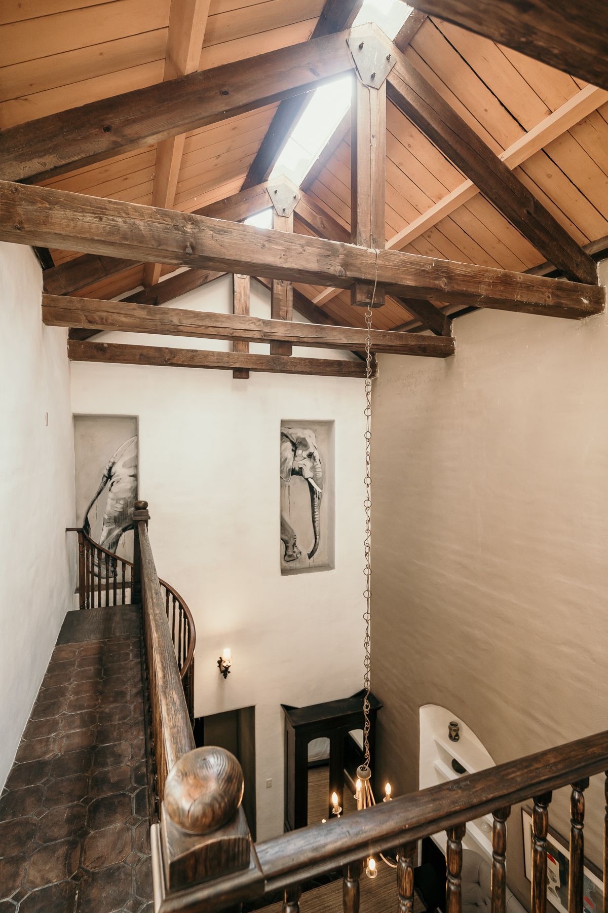 Interior de una casa con vigas de madera a la vista, escalera, arte y luz natural procedente de un tragaluz.