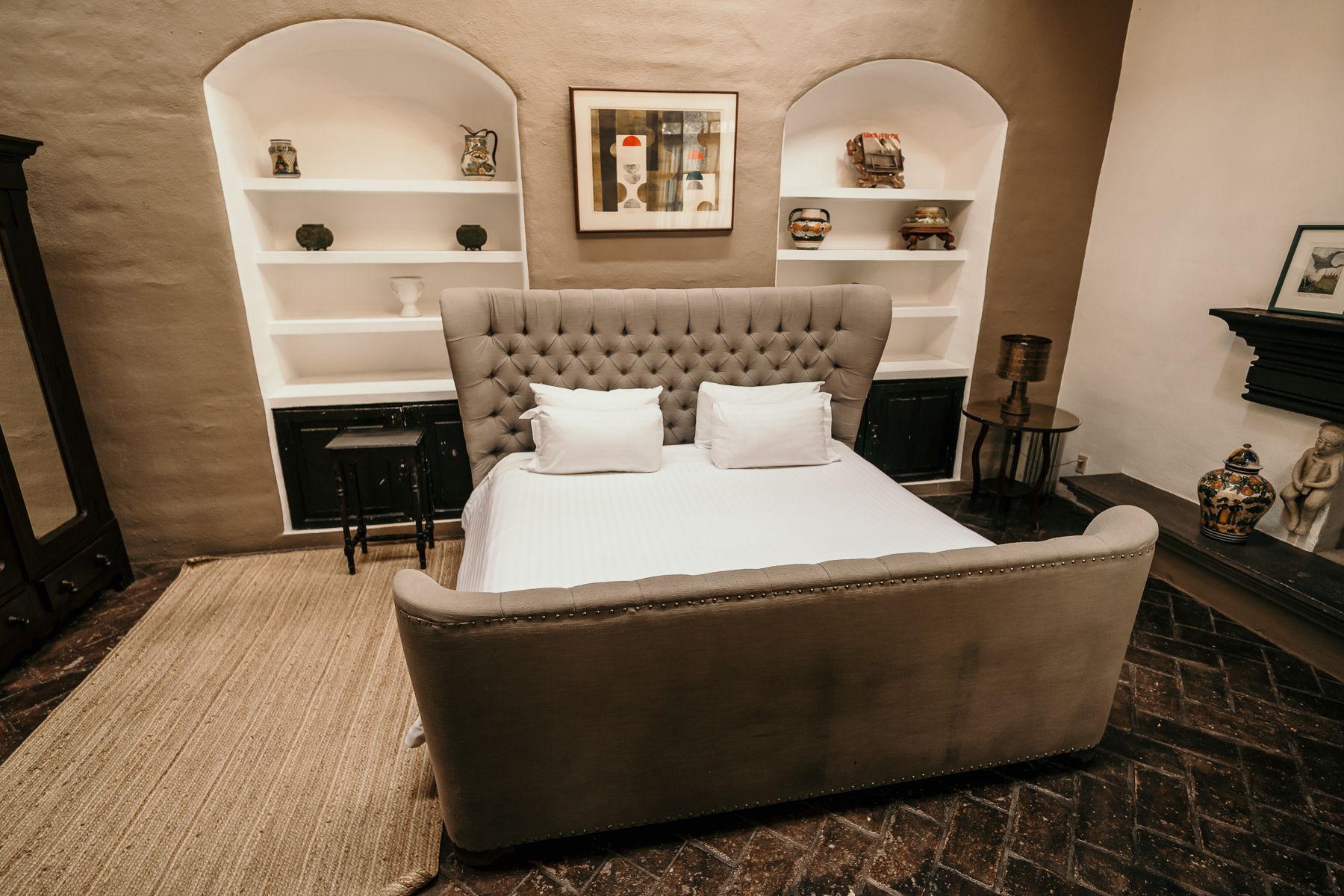 Dormitorio con una cama gris con mechones, ropa de cama blanca, estantes empotrados, obras de arte y una alfombra.