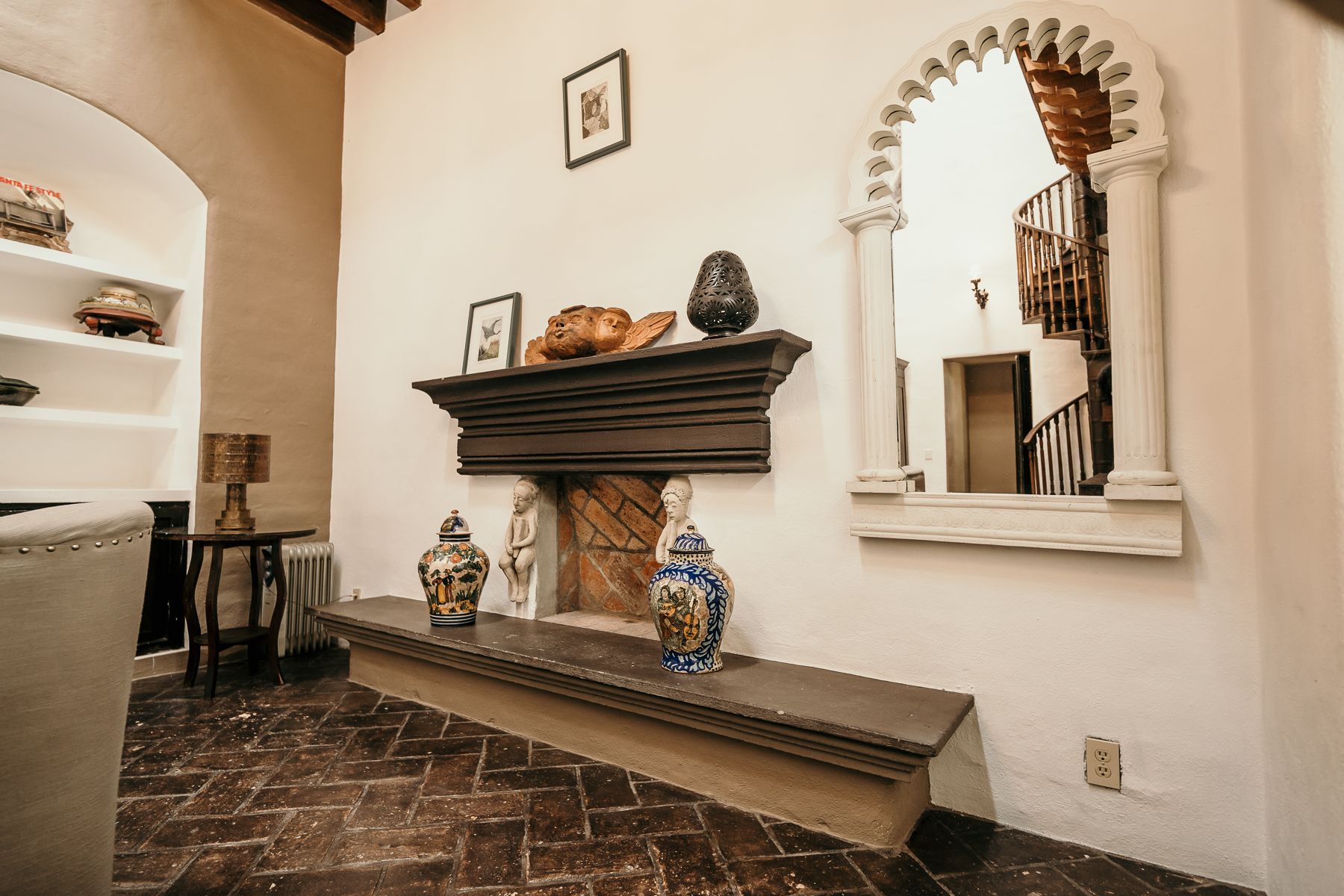 Interior con chimenea, espejo ornamentado, piso de ladrillo y cerámica decorativa.