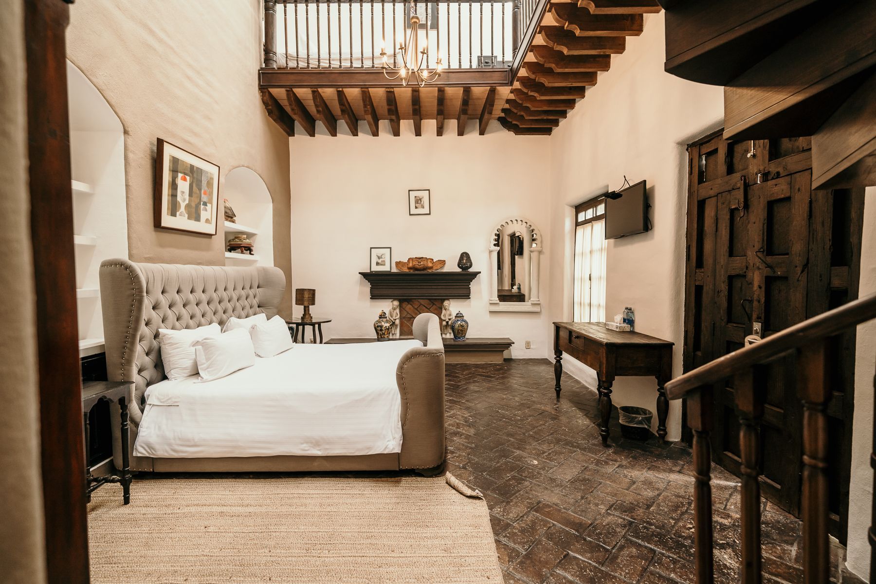 Dormitorio con techo alto, cama grande, chimenea, escalera de madera y balcón.