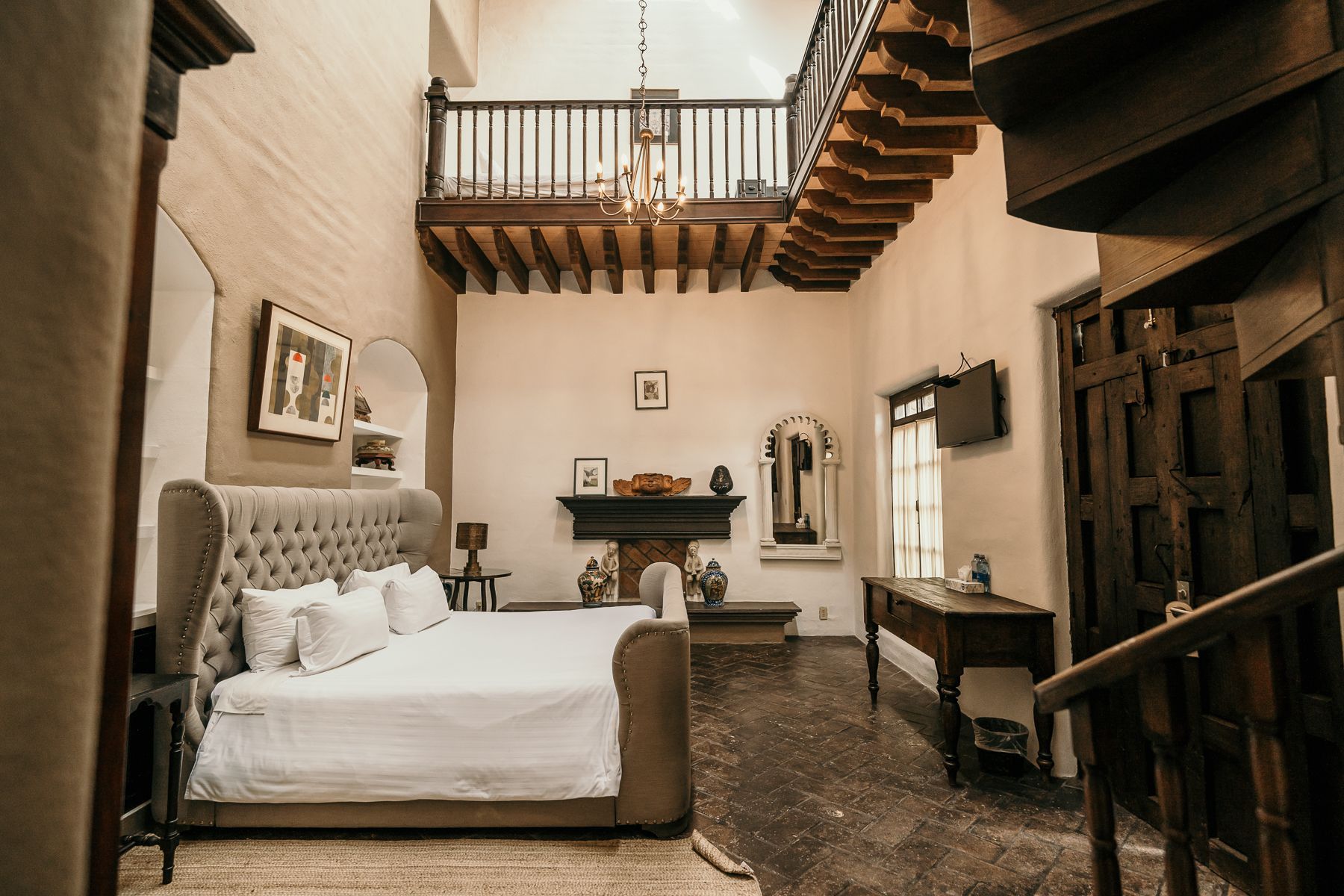 Dormitorio con cama grande, chimenea y balcón. Escalera y suelo de madera oscura.