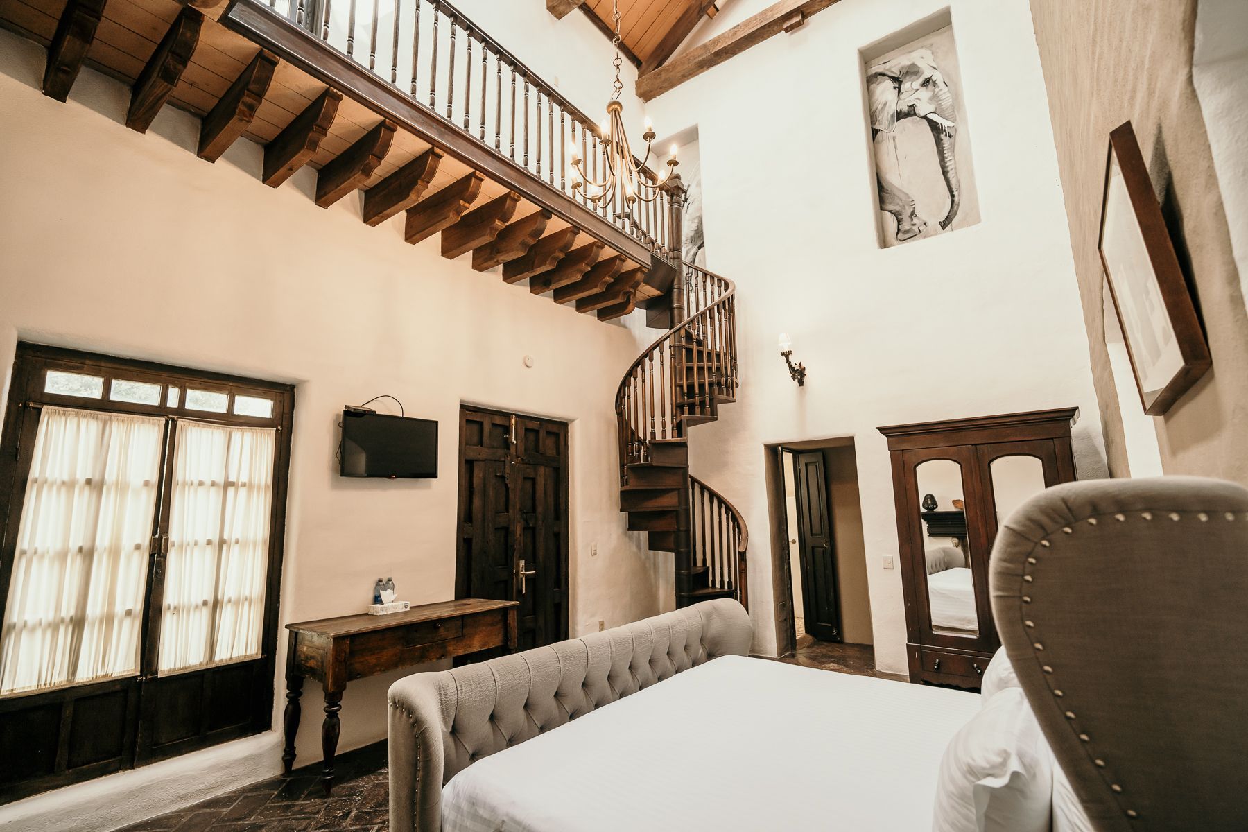 Dormitorio con escalera de caracol, detalles en madera y una cama grande. Paredes blancas y luz natural.