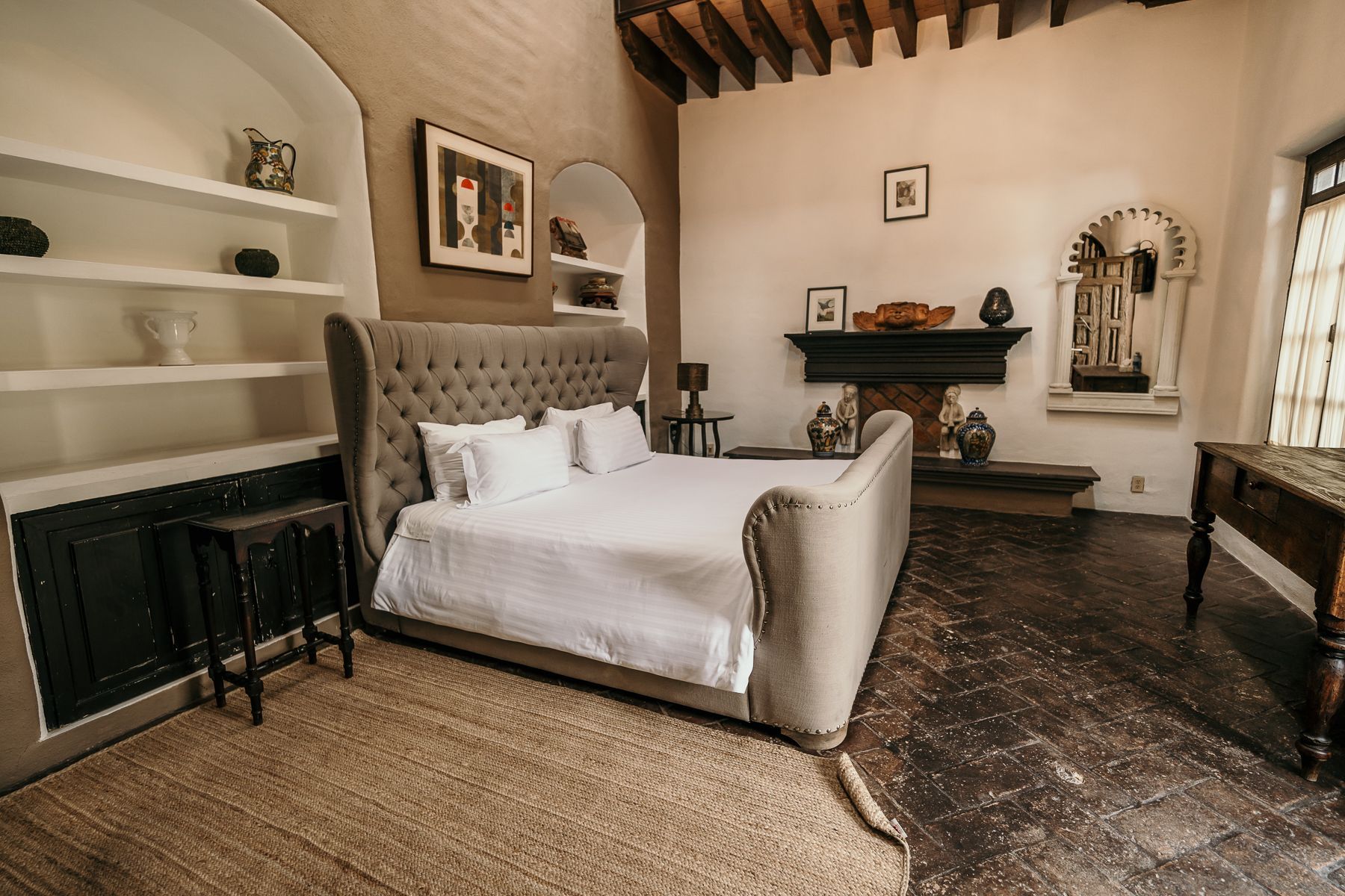 Amplio dormitorio con una gran cama capitoné, chimenea y suelo rústico.