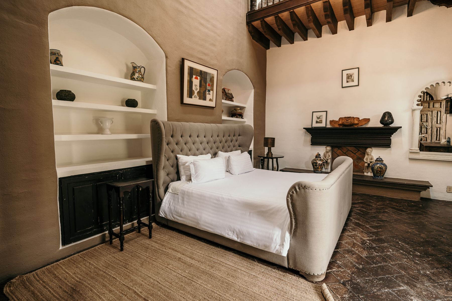 Dormitorio con techos altos, cama grande, estanterías empotradas, chimenea y vigas de madera a la vista.