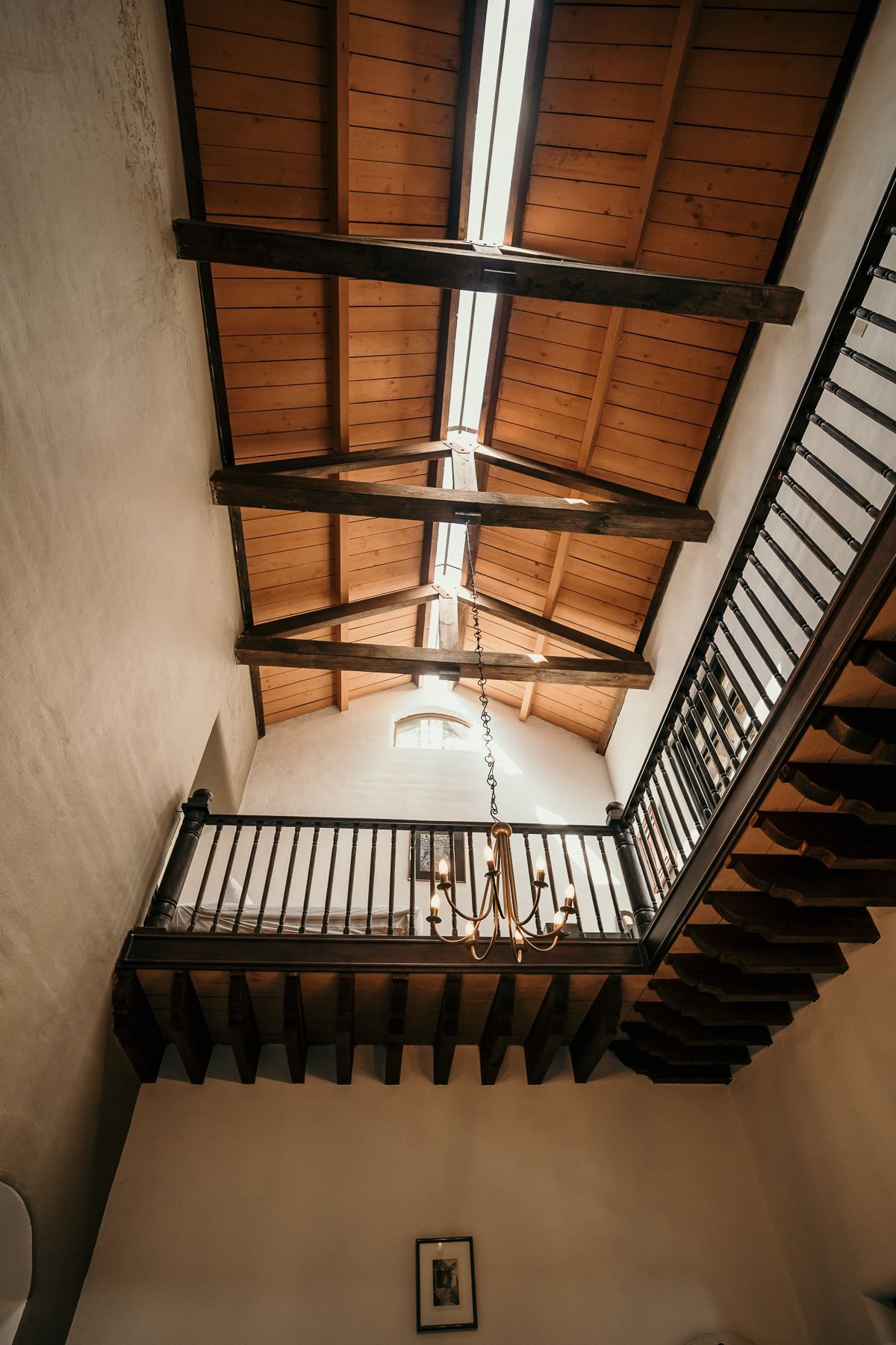Vista interior: Techo con vigas de madera con tragaluz, balcón y escalera.