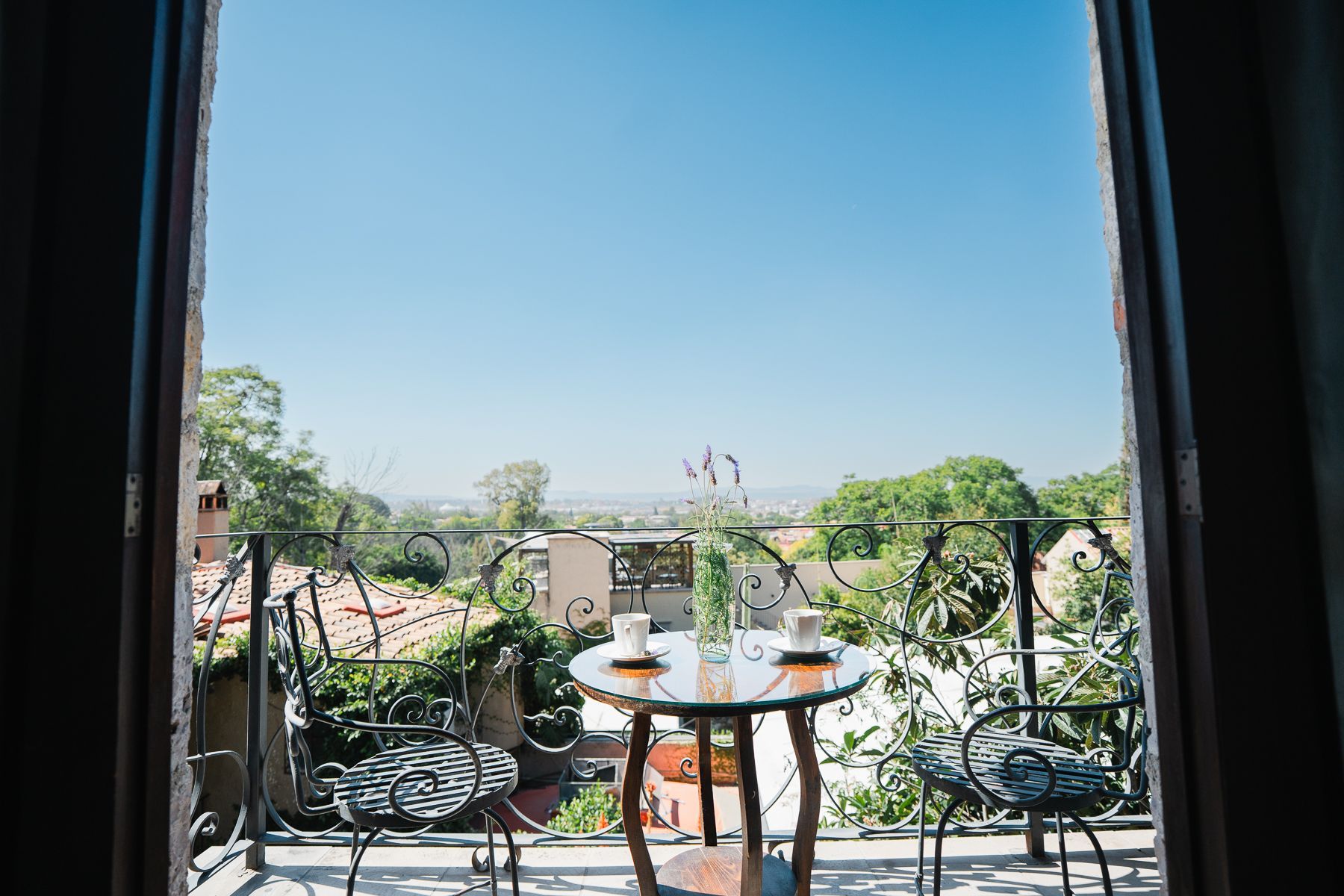 Balcón con mesa, dos sillas y vista del paisaje urbano bajo un cielo azul.