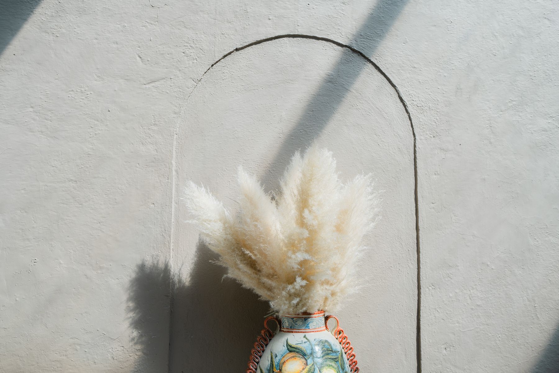 Hierba de la pampa en un jarrón decorativo dentro de un nicho curvo en una pared de estuco gris claro.