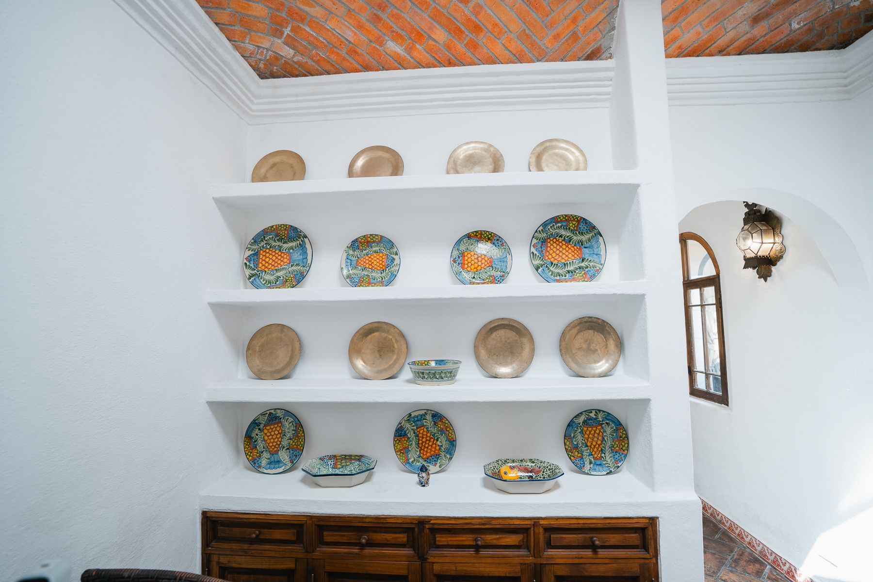 Estantes empotrados de color blanco con placas de cerámica de varios diseños; mueble de madera marrón debajo.