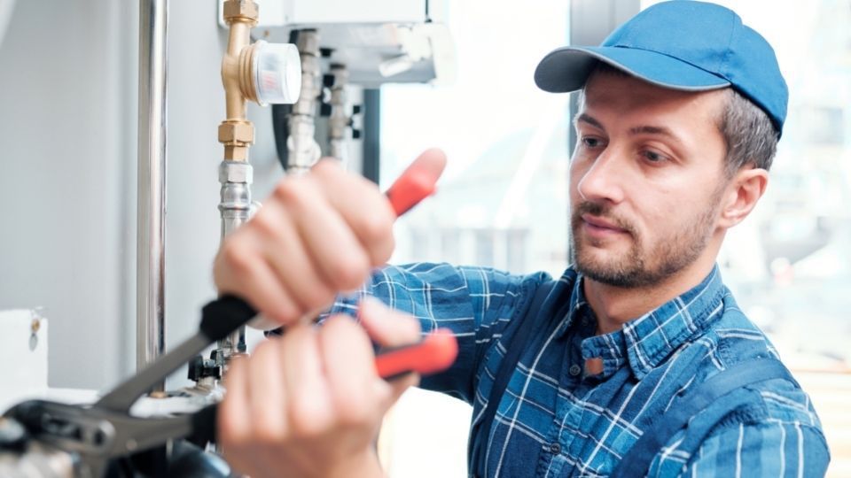 a plumber in a blue hat and shirt using a wrench to fix a pipe