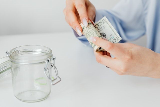 hand placing rolled up twenty dollar bills in a jar