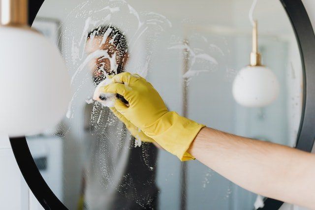 person in yellow cleaning gloves scrubbing a black-framed mirror