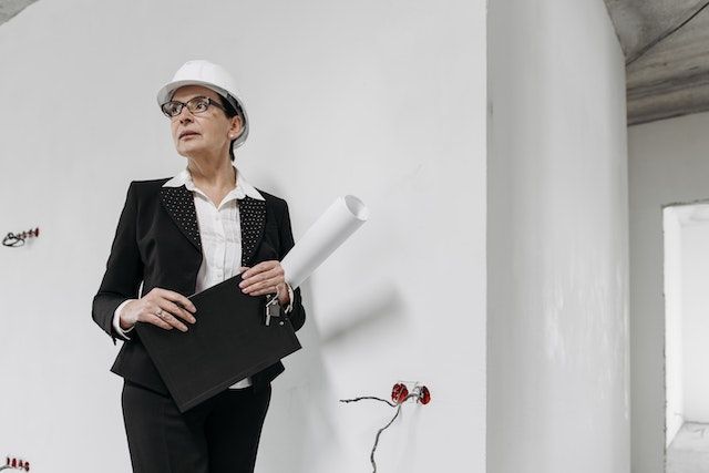 property inspector in a black suit and white hardhat looking at new electrical work
