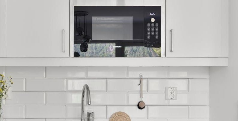 A kitchen with white cabinets , a sink , and a microwave.
