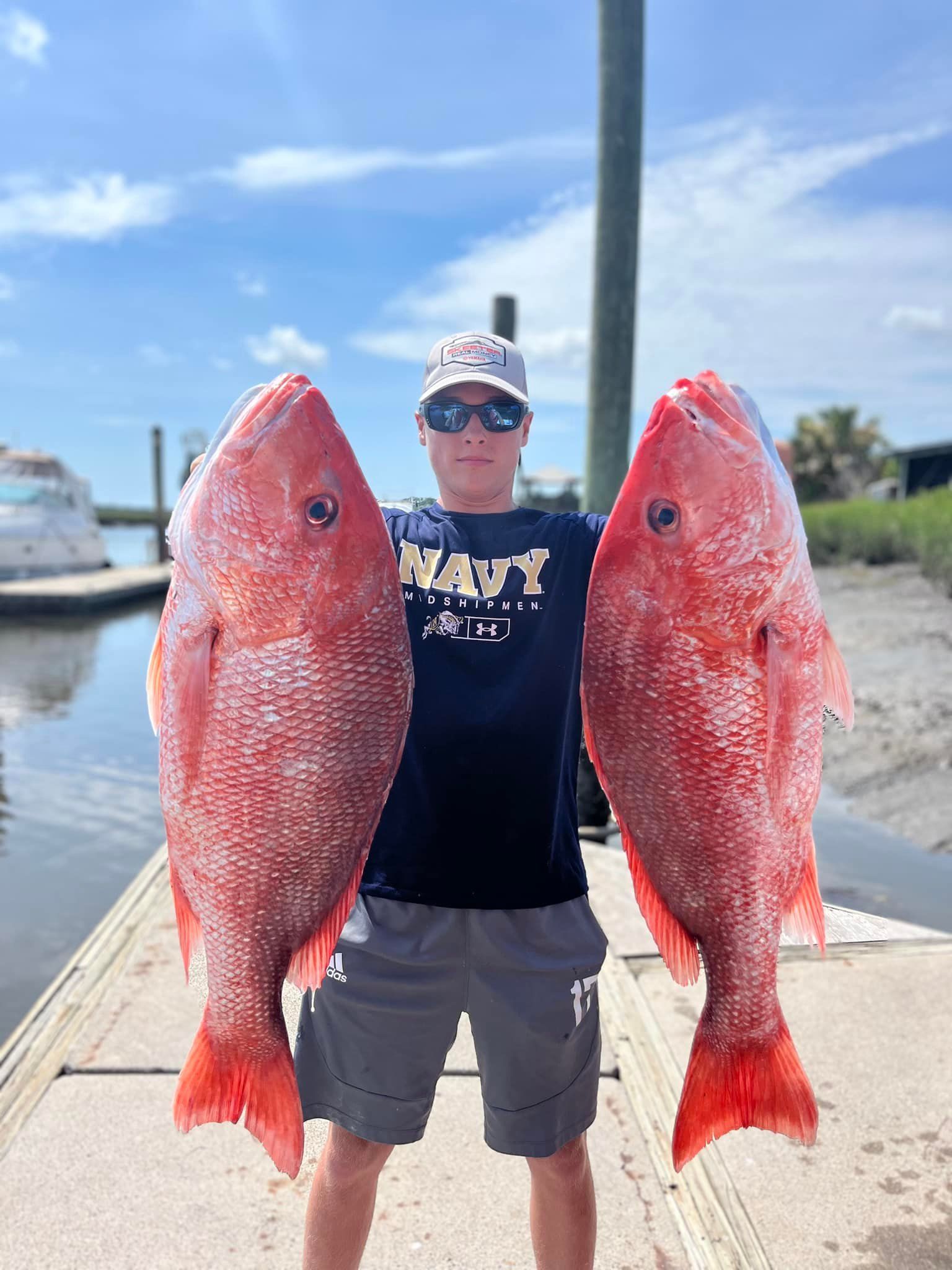 A man is holding two large red fish on a dock.