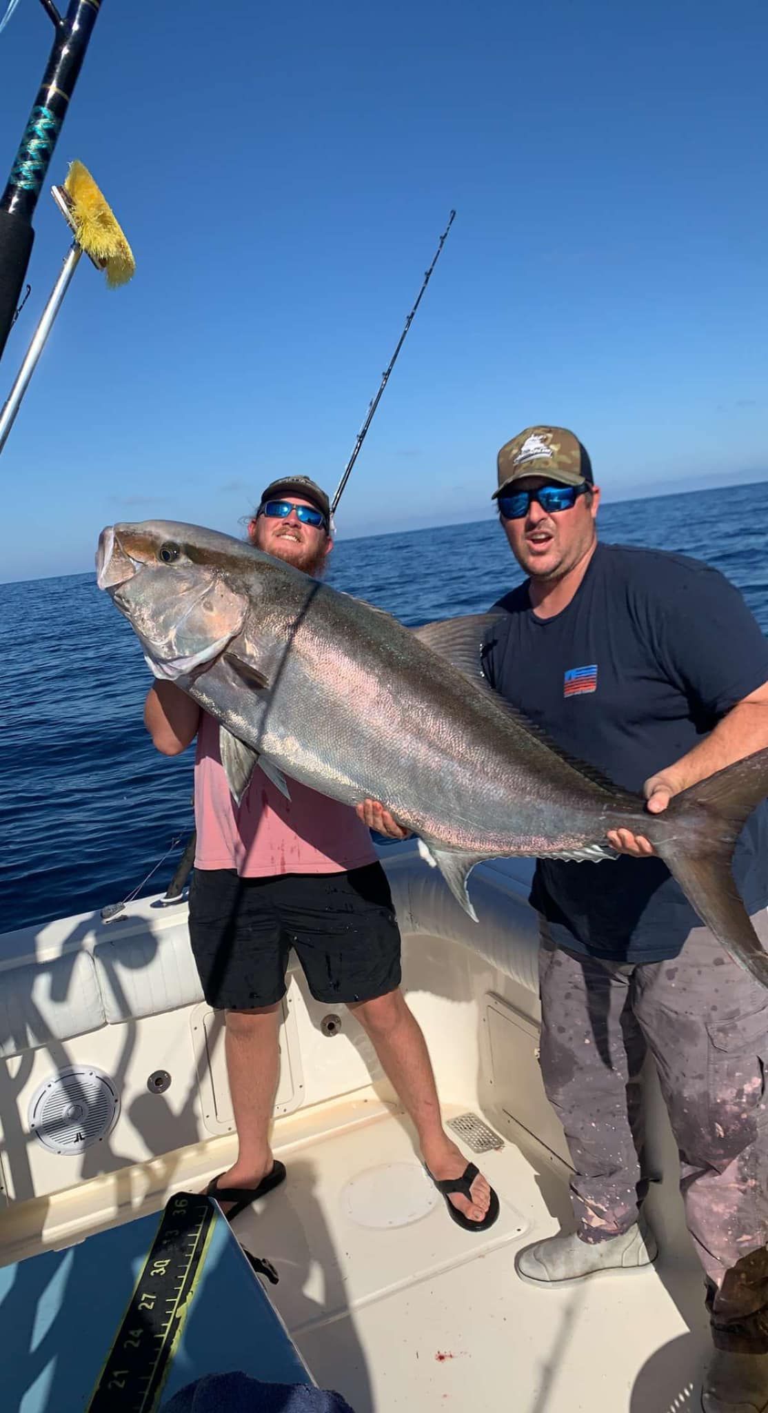 Two men are standing on a boat holding a large fish.