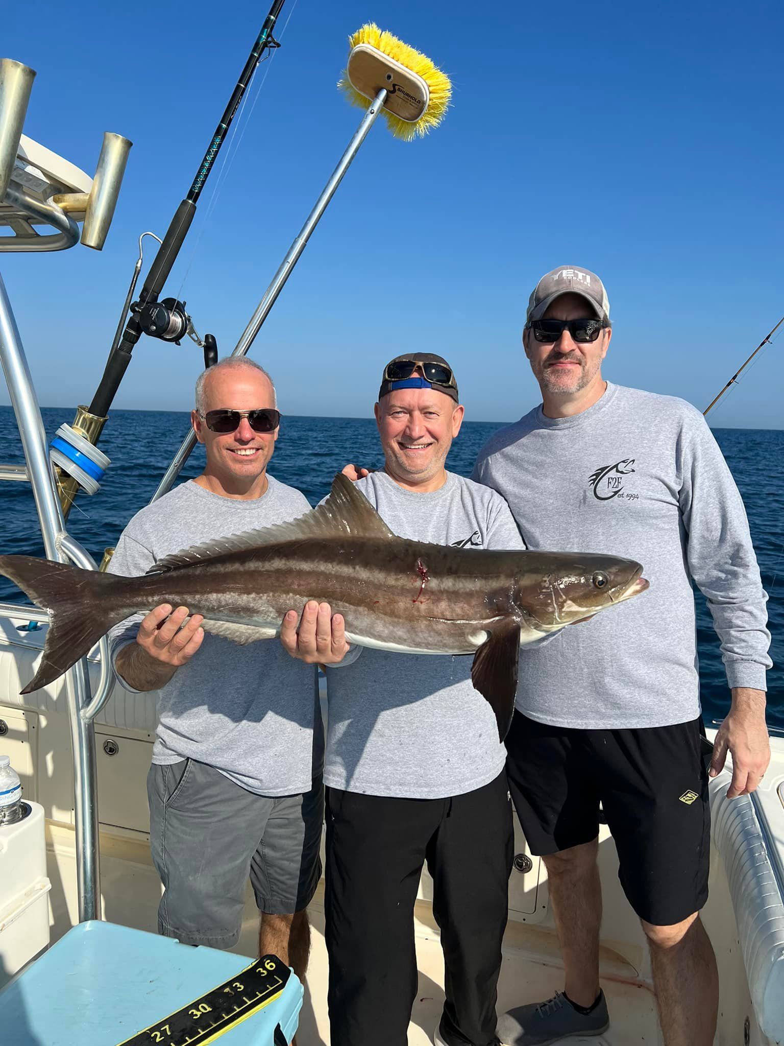 Three men are standing on a boat holding a large fish.