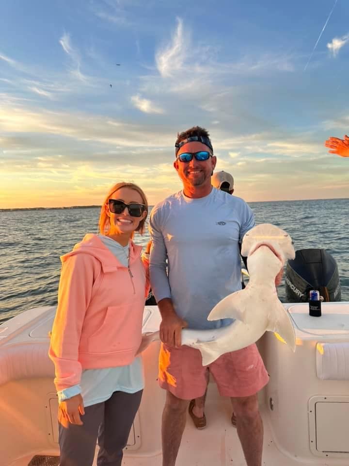 A man and a woman are standing on a boat holding a stuffed shark.