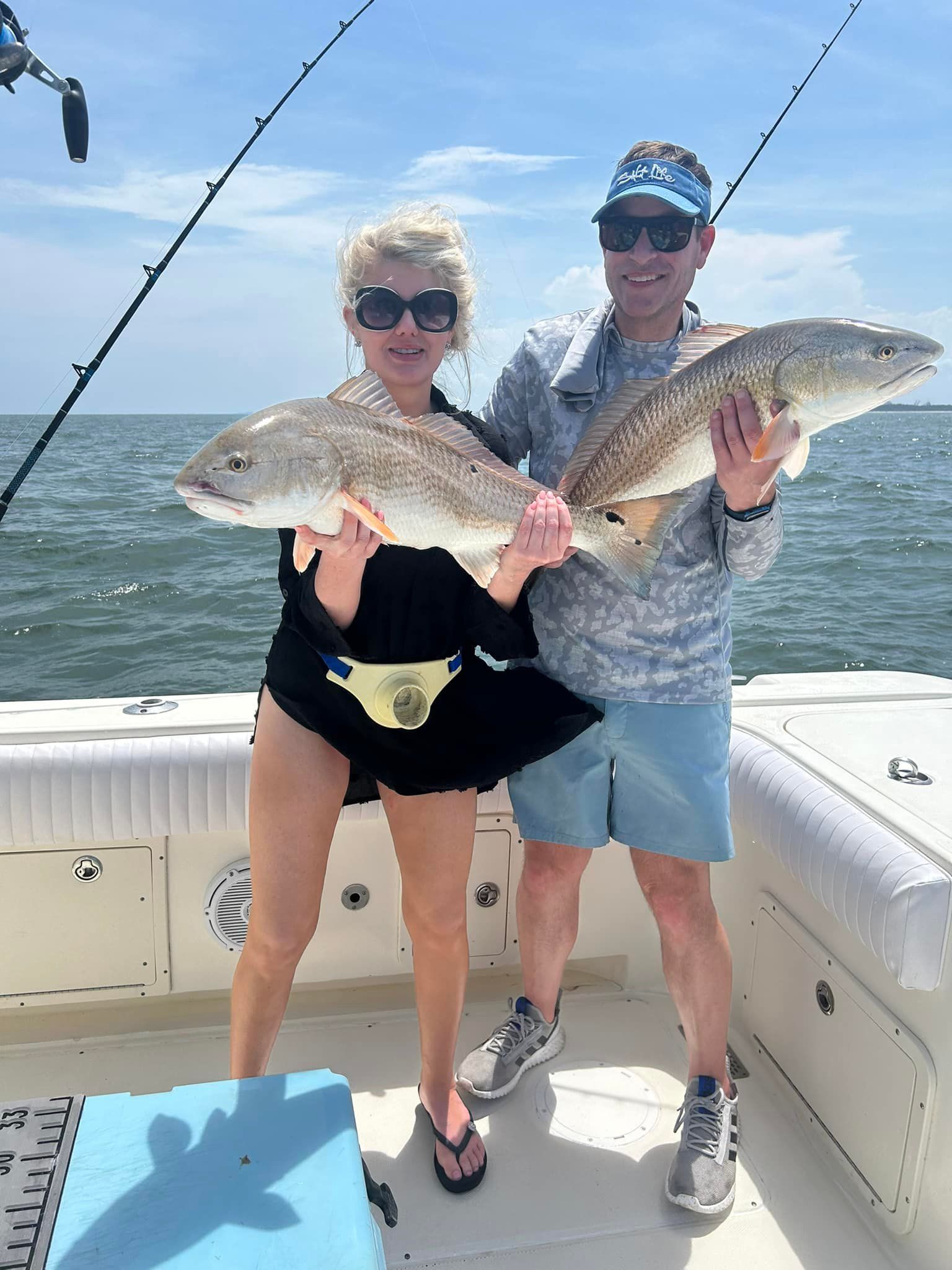 A man and a woman are holding two large fish on a boat.