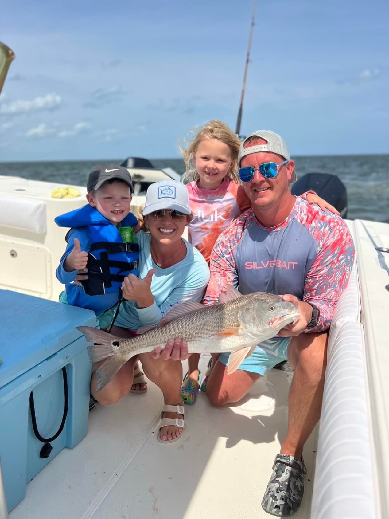 A family is sitting on a boat holding a large fish.