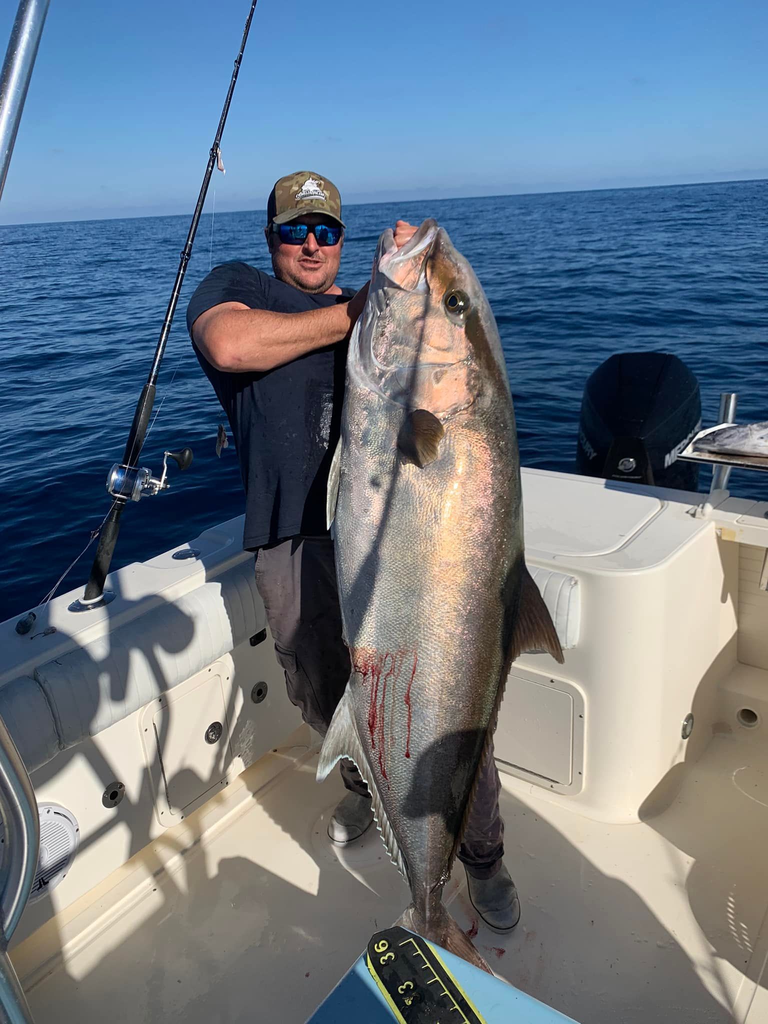 A man is holding a large fish on a boat in the ocean.