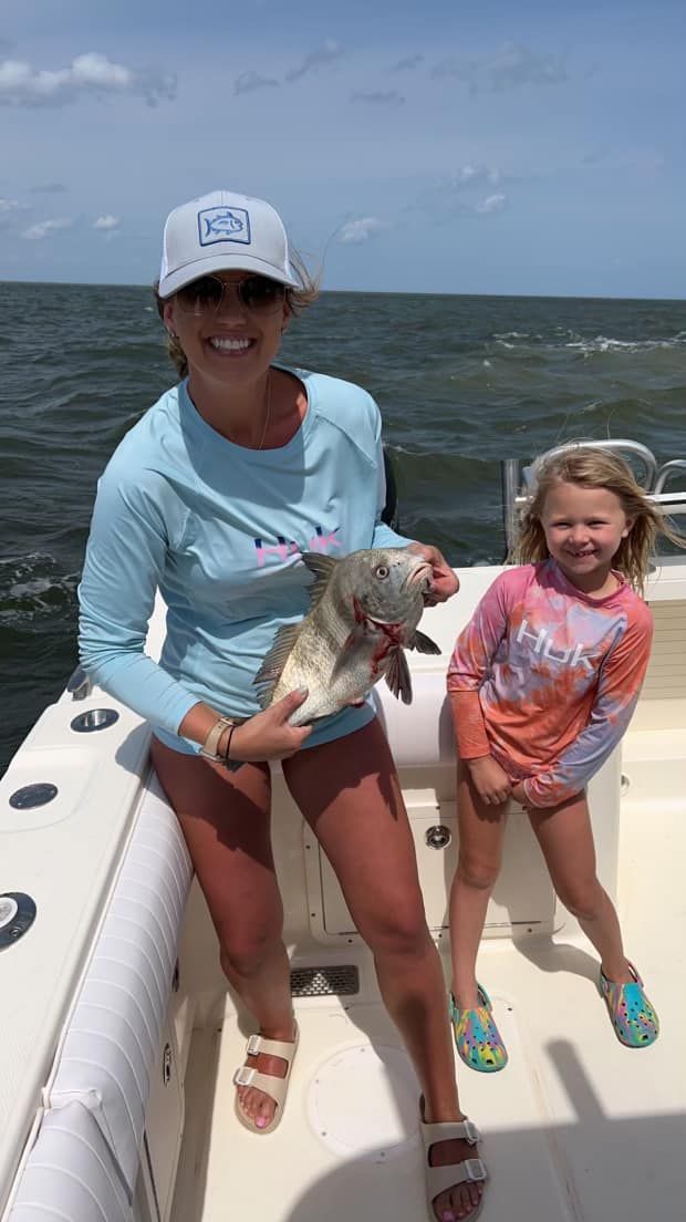 A woman and a little girl are standing on a boat holding a fish.