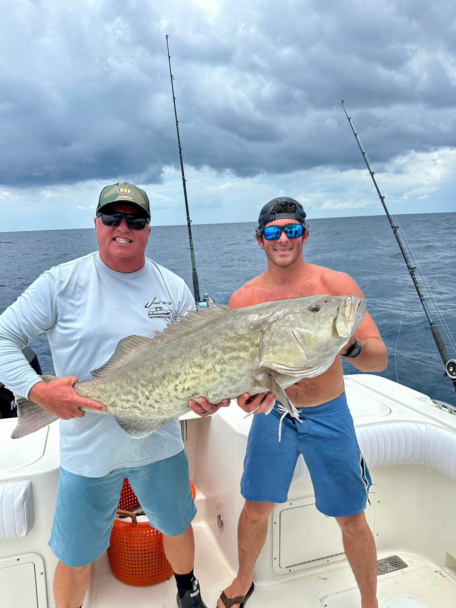 Two men are standing on a boat holding a large fish.