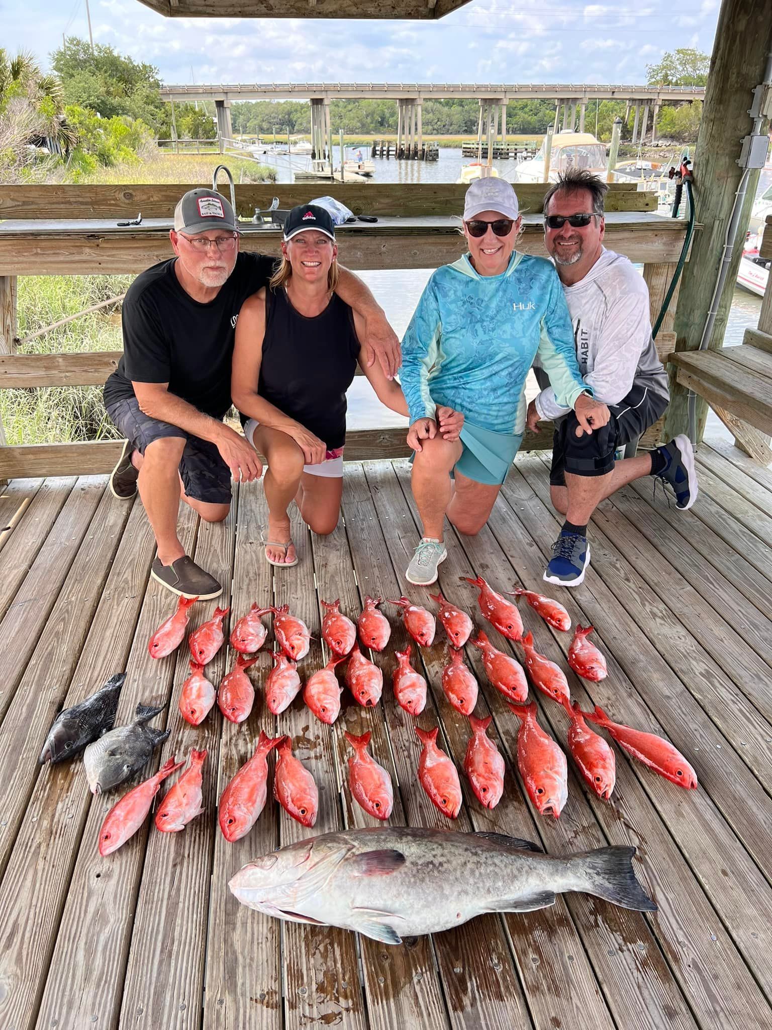 A group of people are posing for a picture with a large fish on a wooden deck.