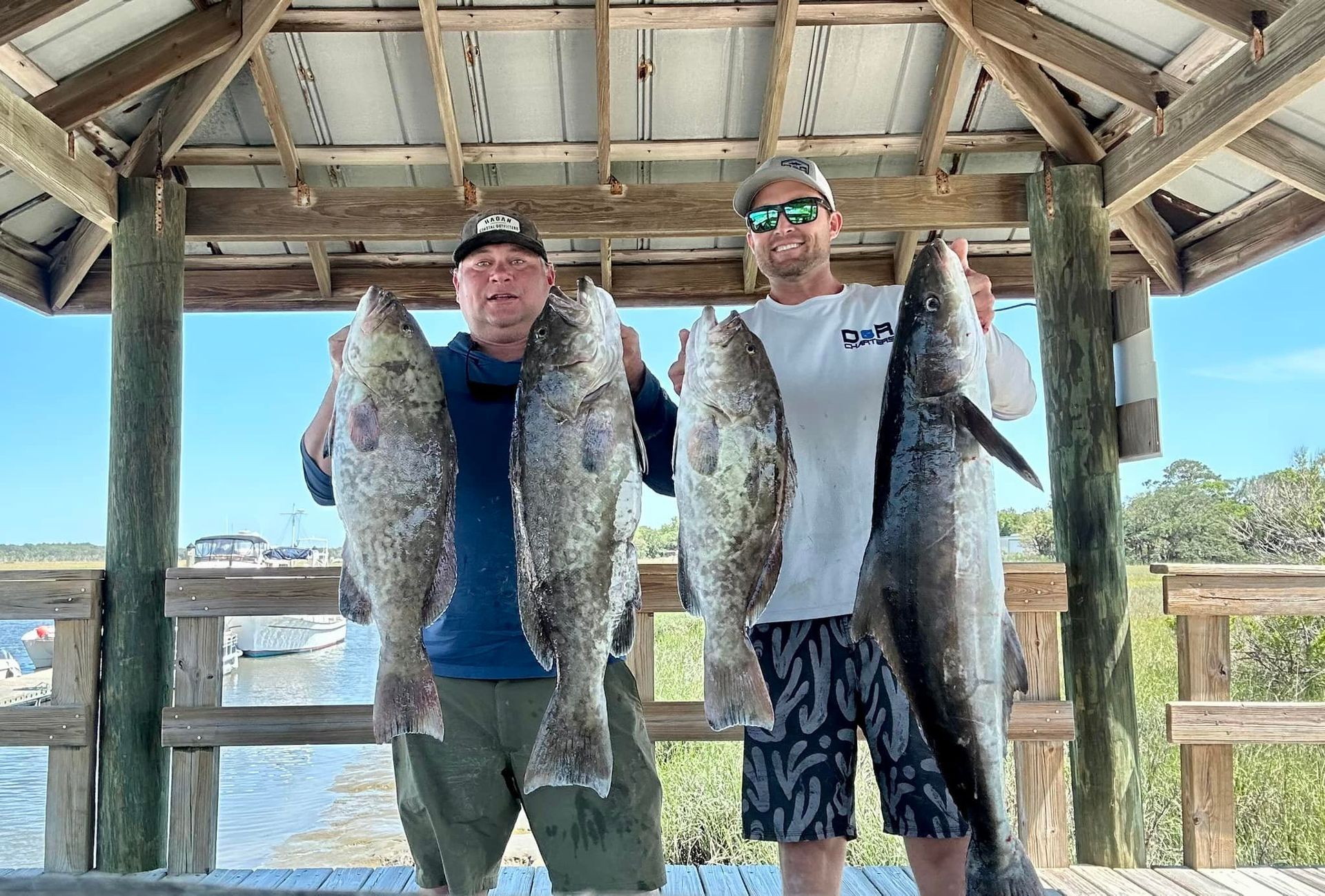 Two men are standing under a gazebo holding fish.