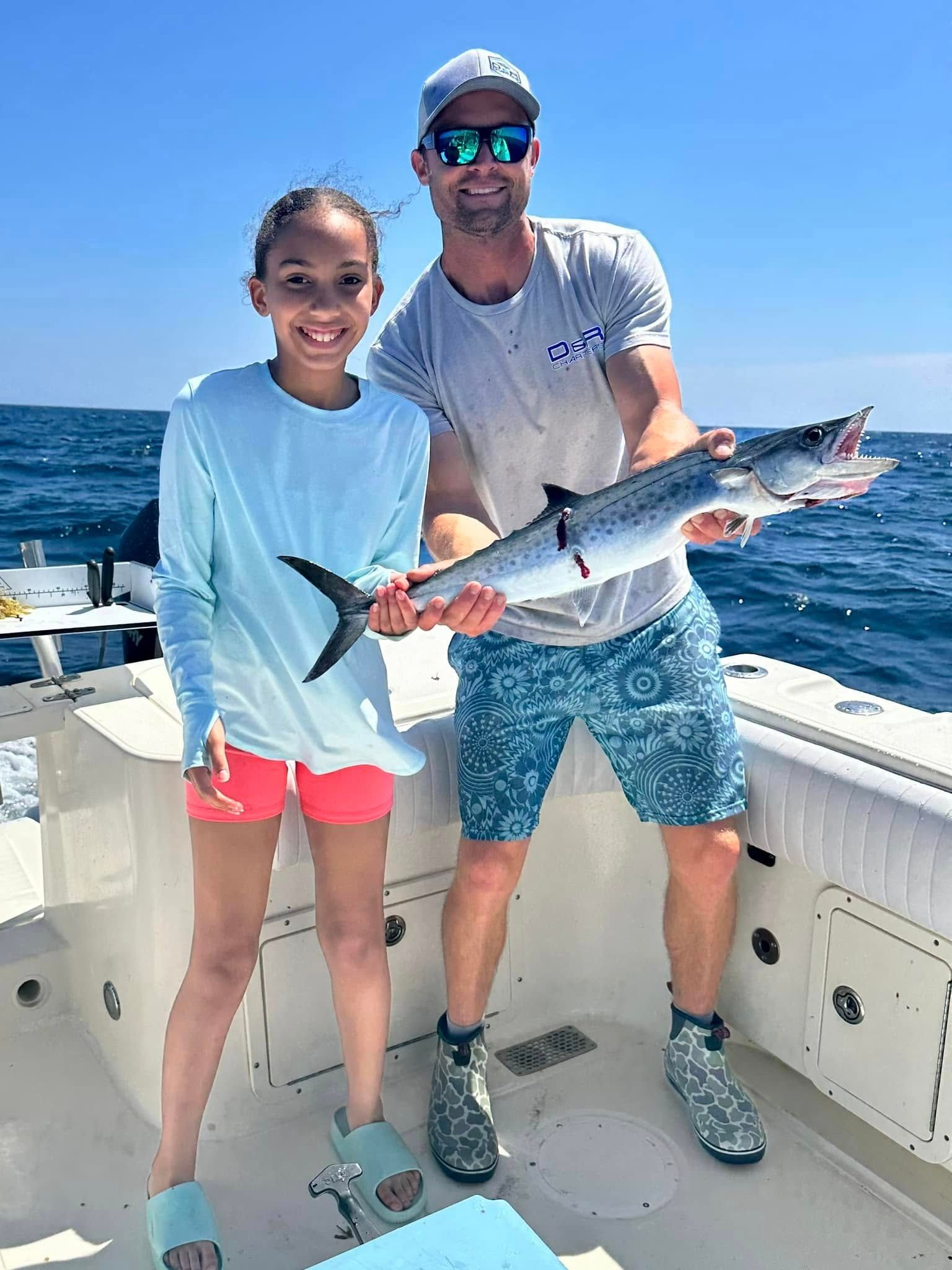 A man and a girl are standing on a boat holding a fish.