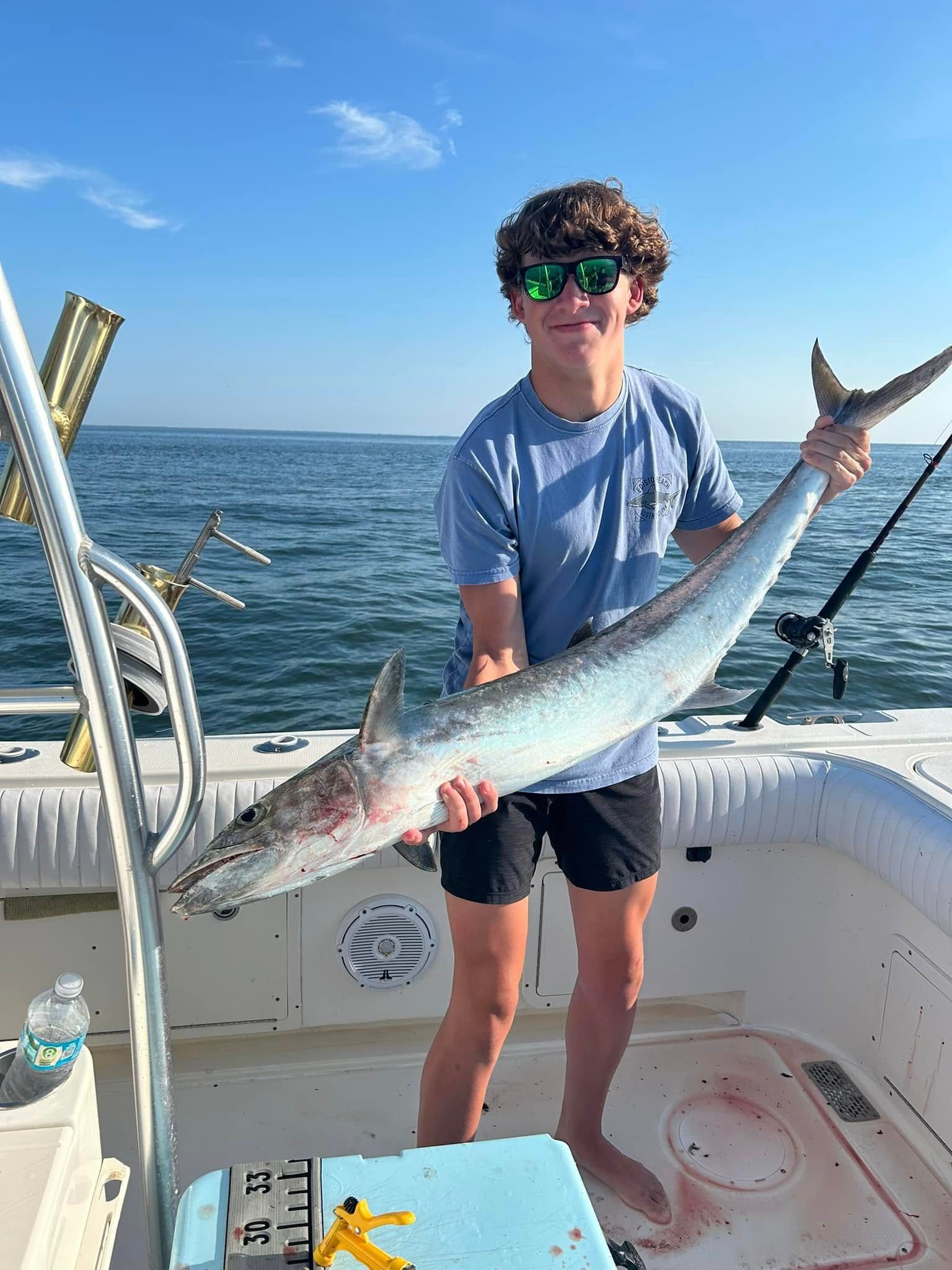 A young man is holding a large fish on a boat.