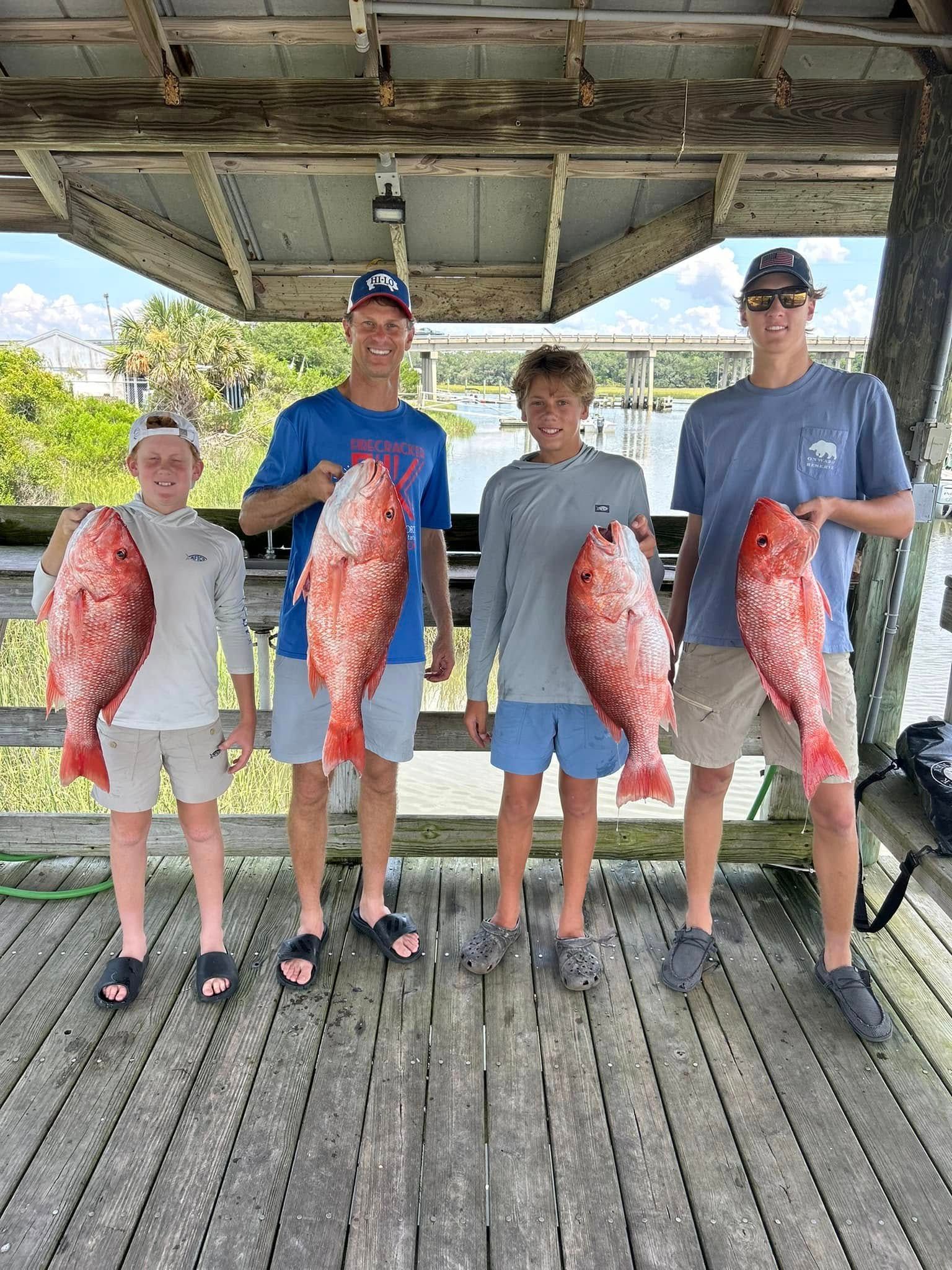 A group of young men are standing on a wooden deck holding large fish.