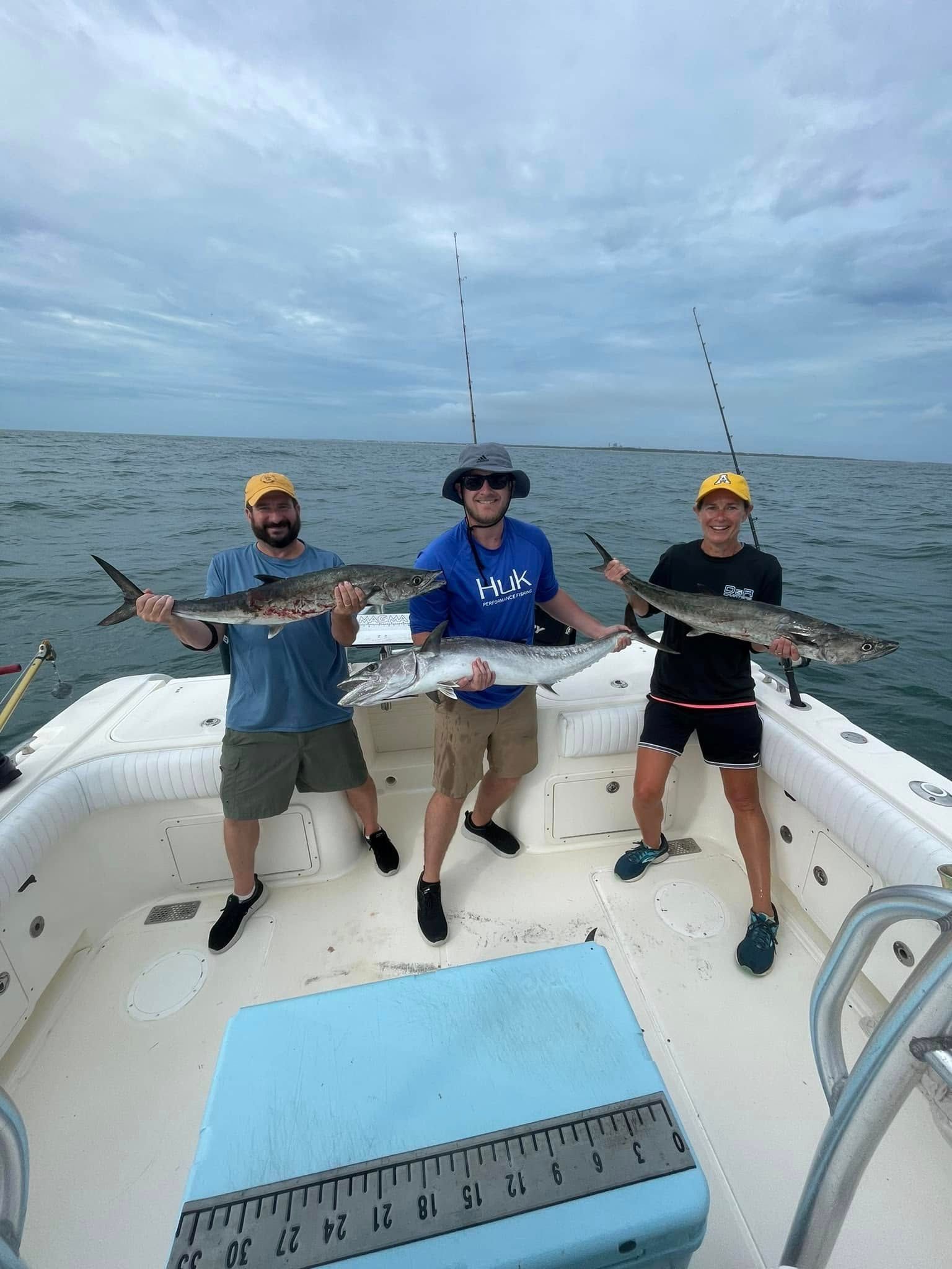 Three men are standing on a boat holding fish.