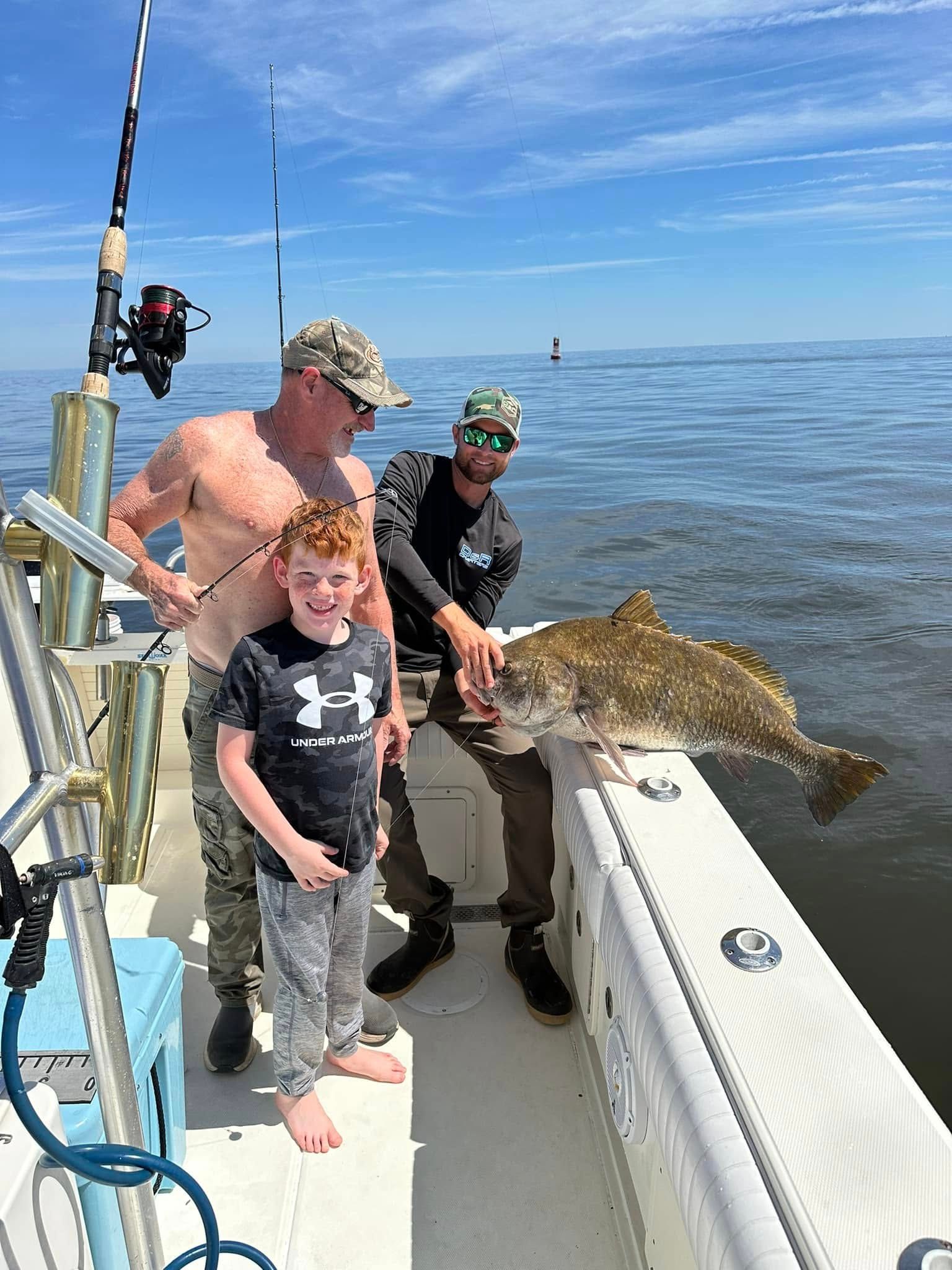 Two men and a boy are standing on a boat holding a large fish.