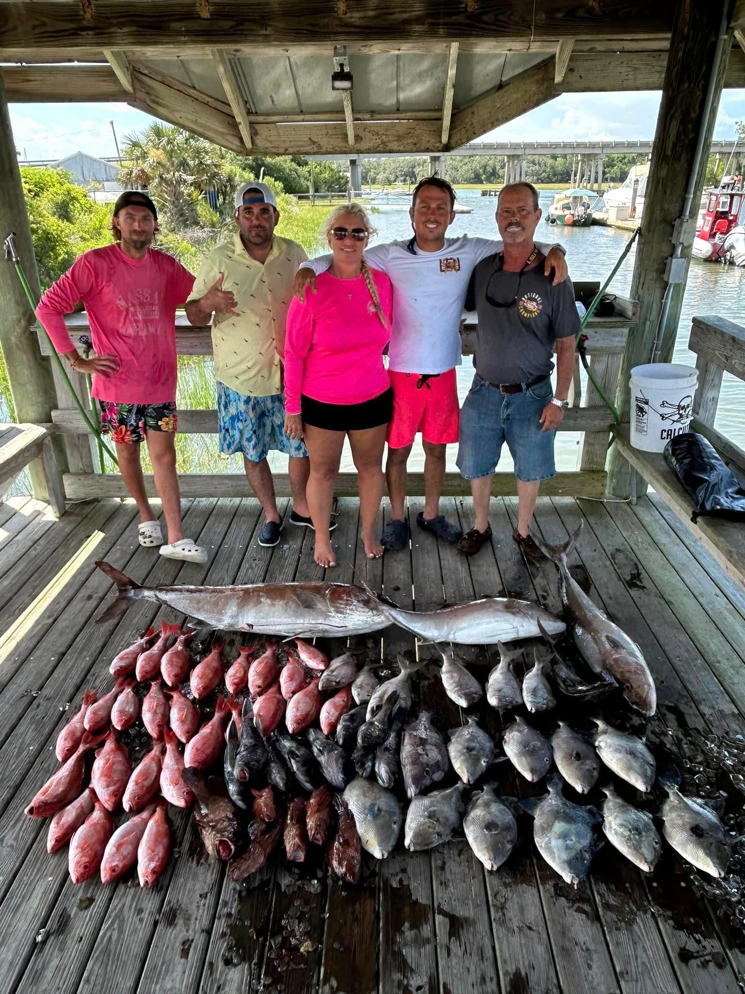 A group of people standing next to a pile of fish on a wooden deck.