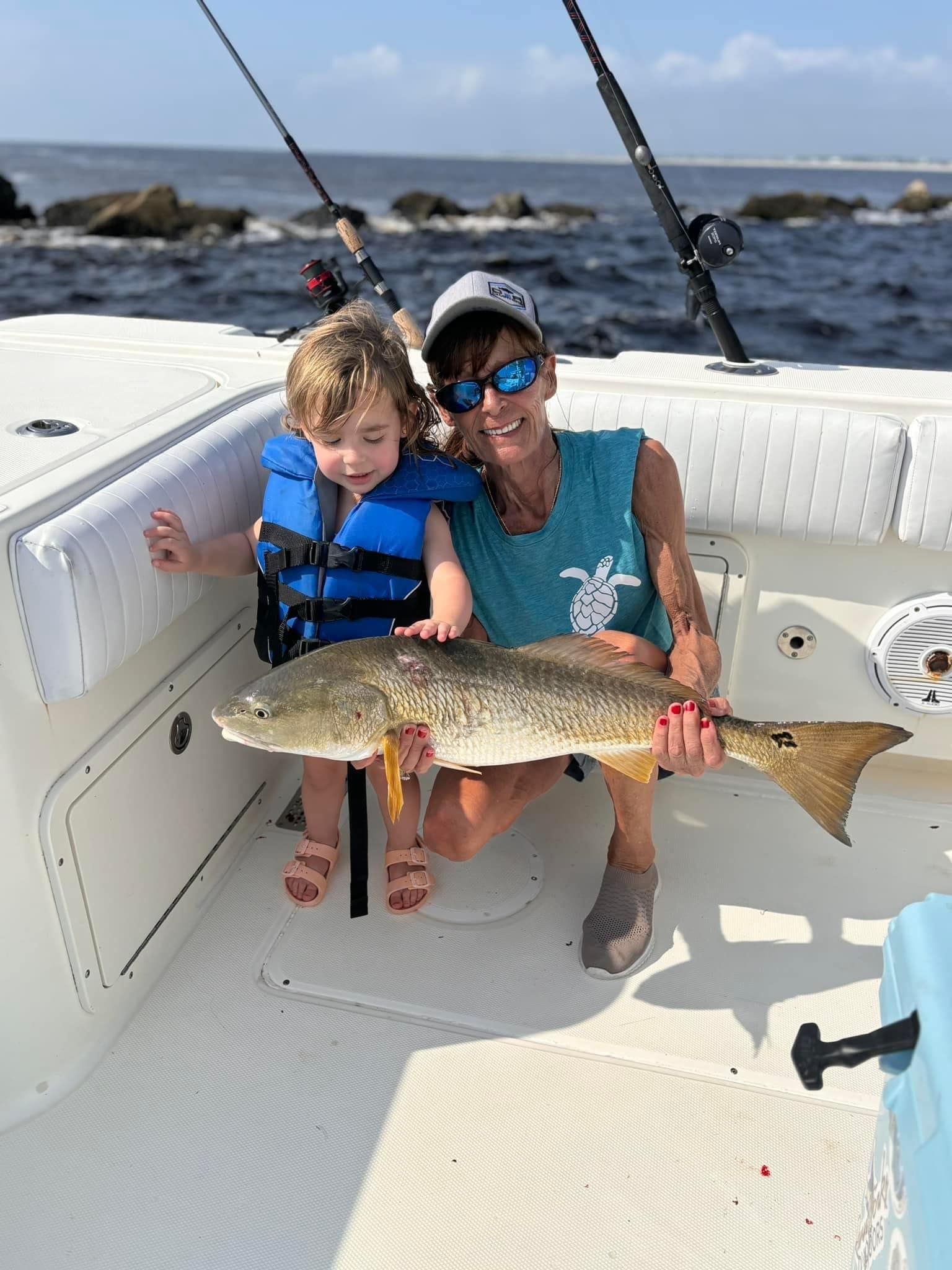 A woman and a child are sitting on a boat holding a large fish.