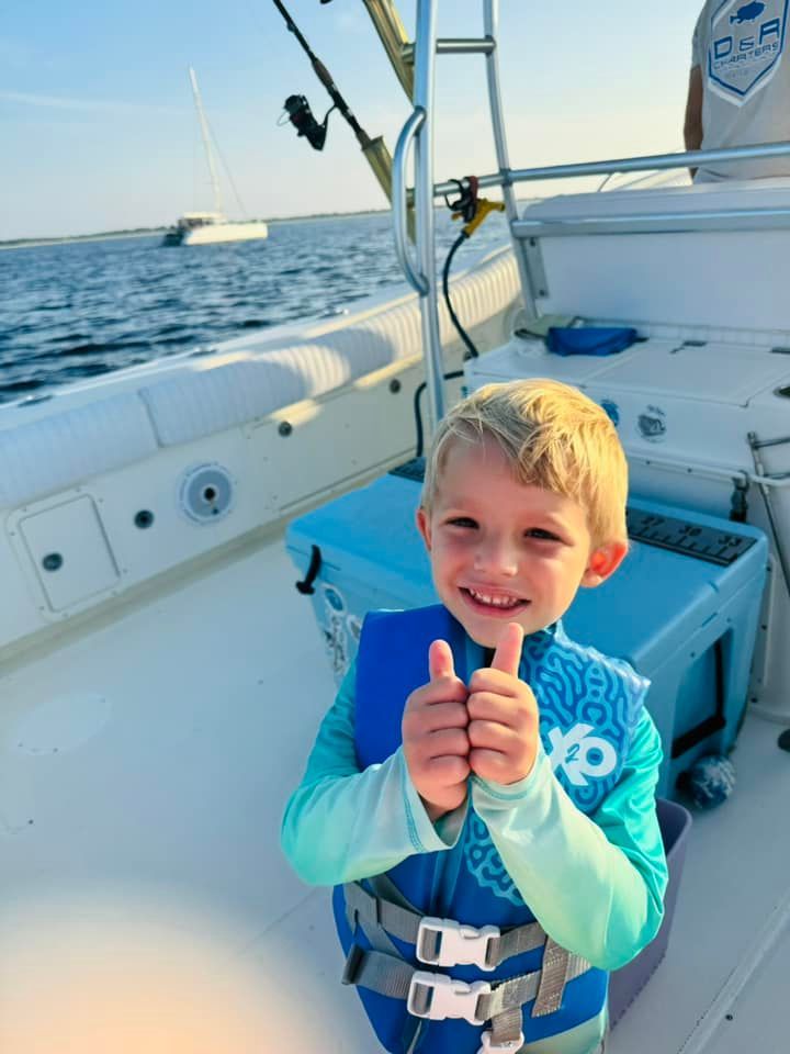 A young boy wearing a life vest is giving a thumbs up on a boat