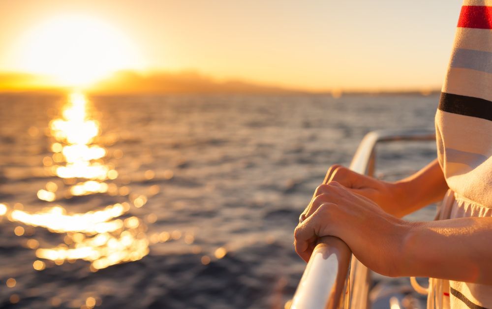 A woman is standing on a boat looking at the sunset over the ocean.