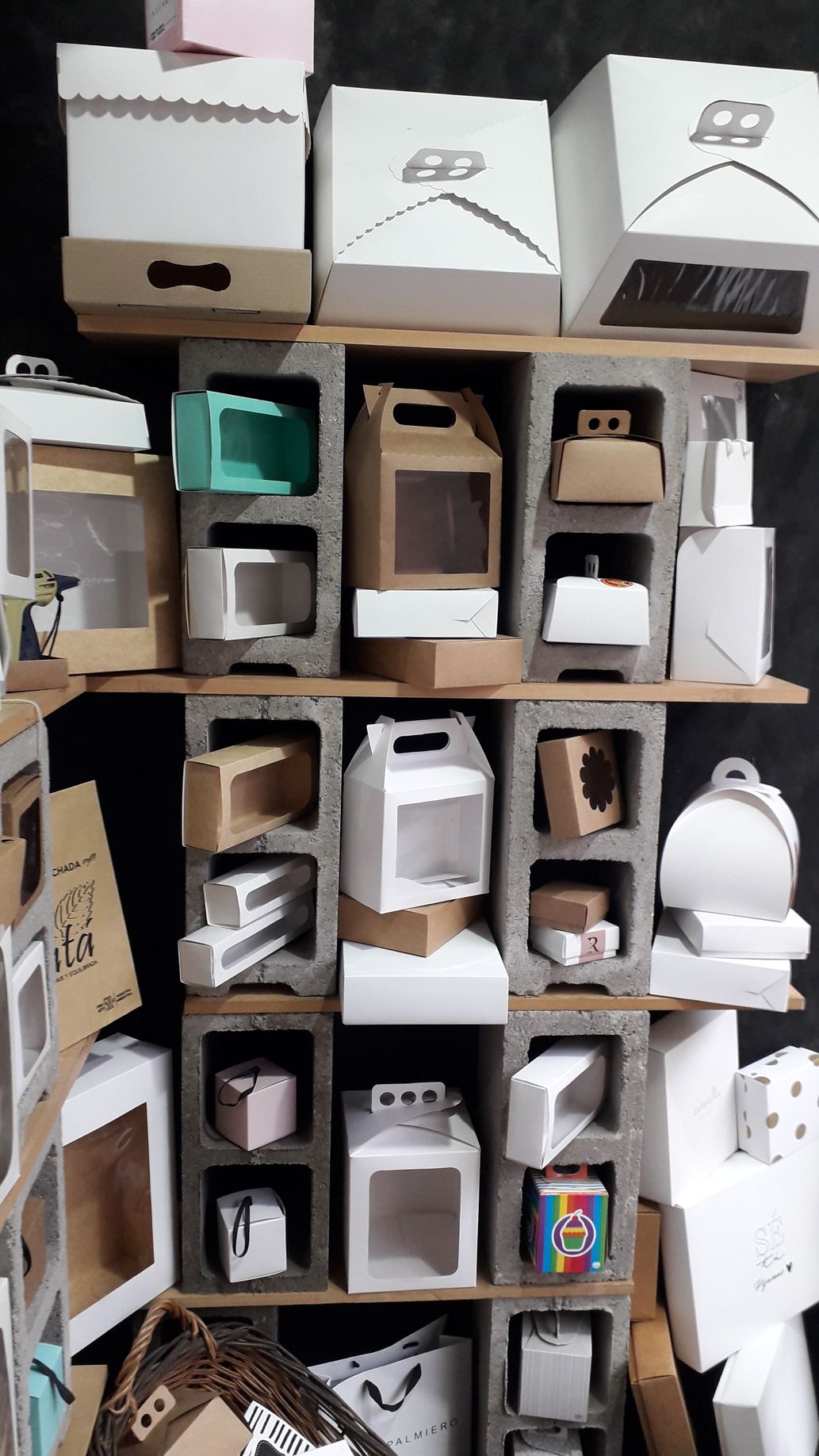 Una exhibición de diversas cajas de cartón para panadería y regalos apiladas en estantes de bloques de hormigón gris.