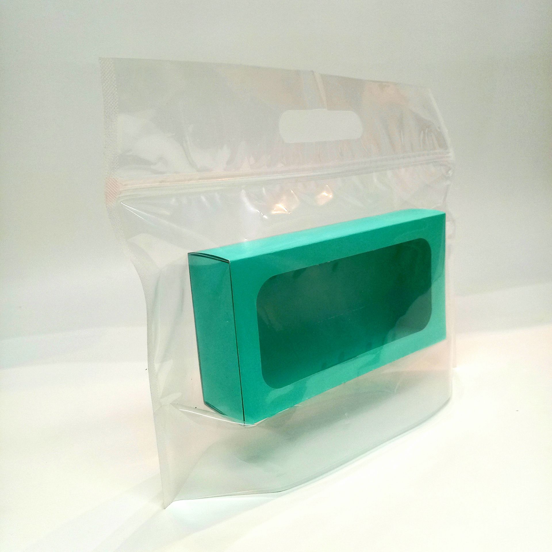 Una bolsa de plástico transparente con cierre de cremallera que contiene una pequeña caja rectangular de color verde azulado.