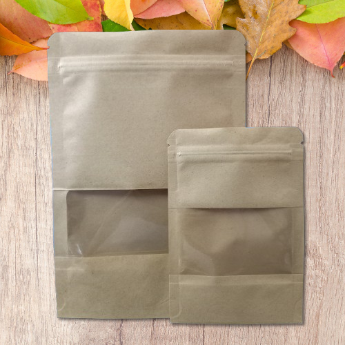 Dos bolsas de papel kraft color tostado con ventana transparente, colocadas sobre un fondo de madera.